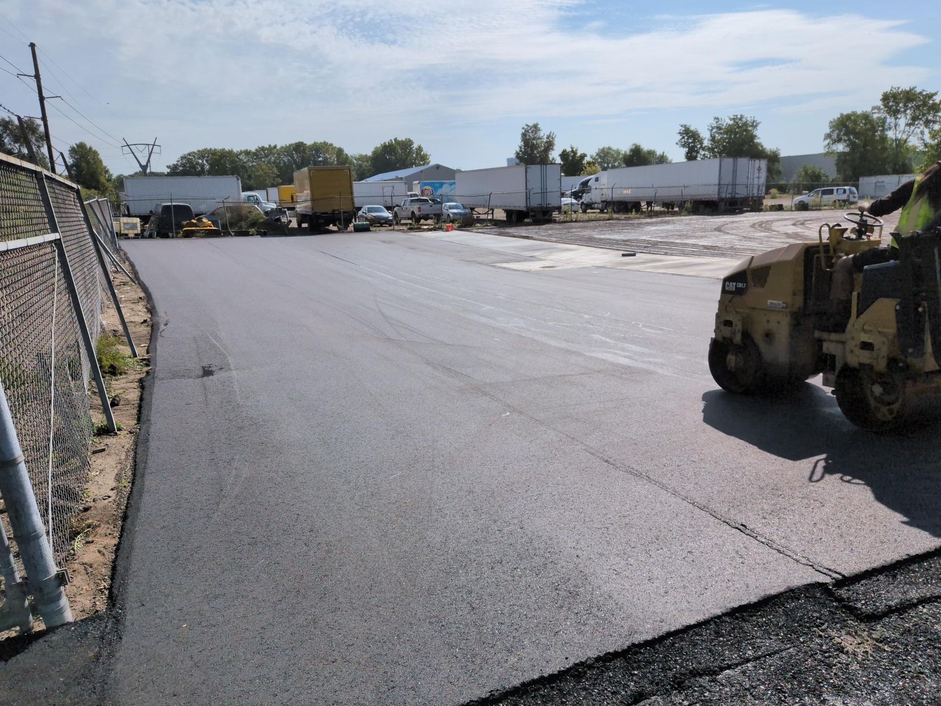 Military vehicle in a paved lot near trailers and fences under a clear sky