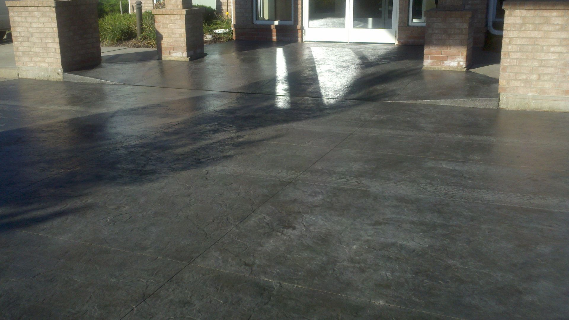 Wet concrete driveway leading to a brick building entrance with bright sunlight reflections.