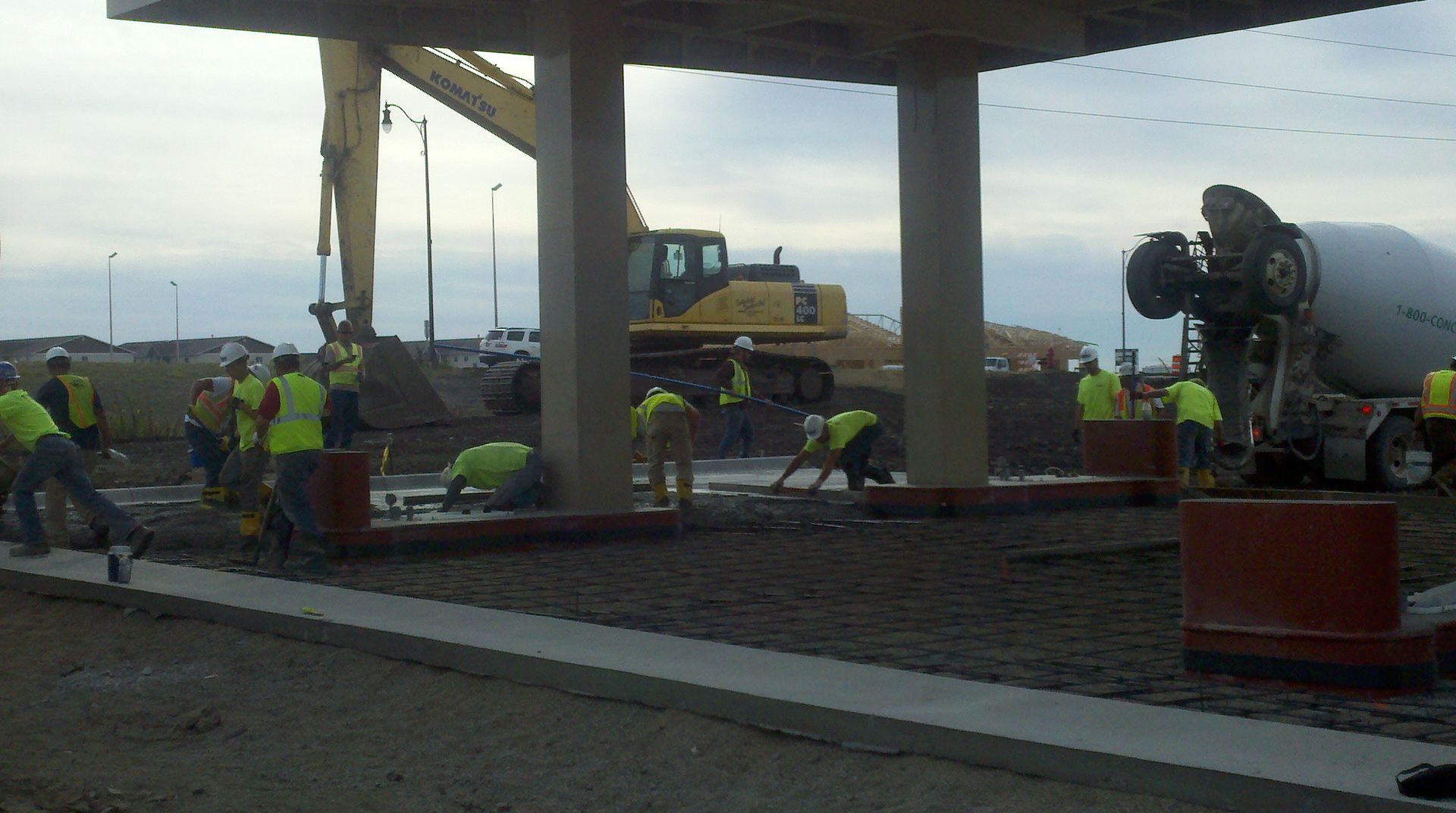 Construction workers and machinery at a roadside building site under a concrete structure