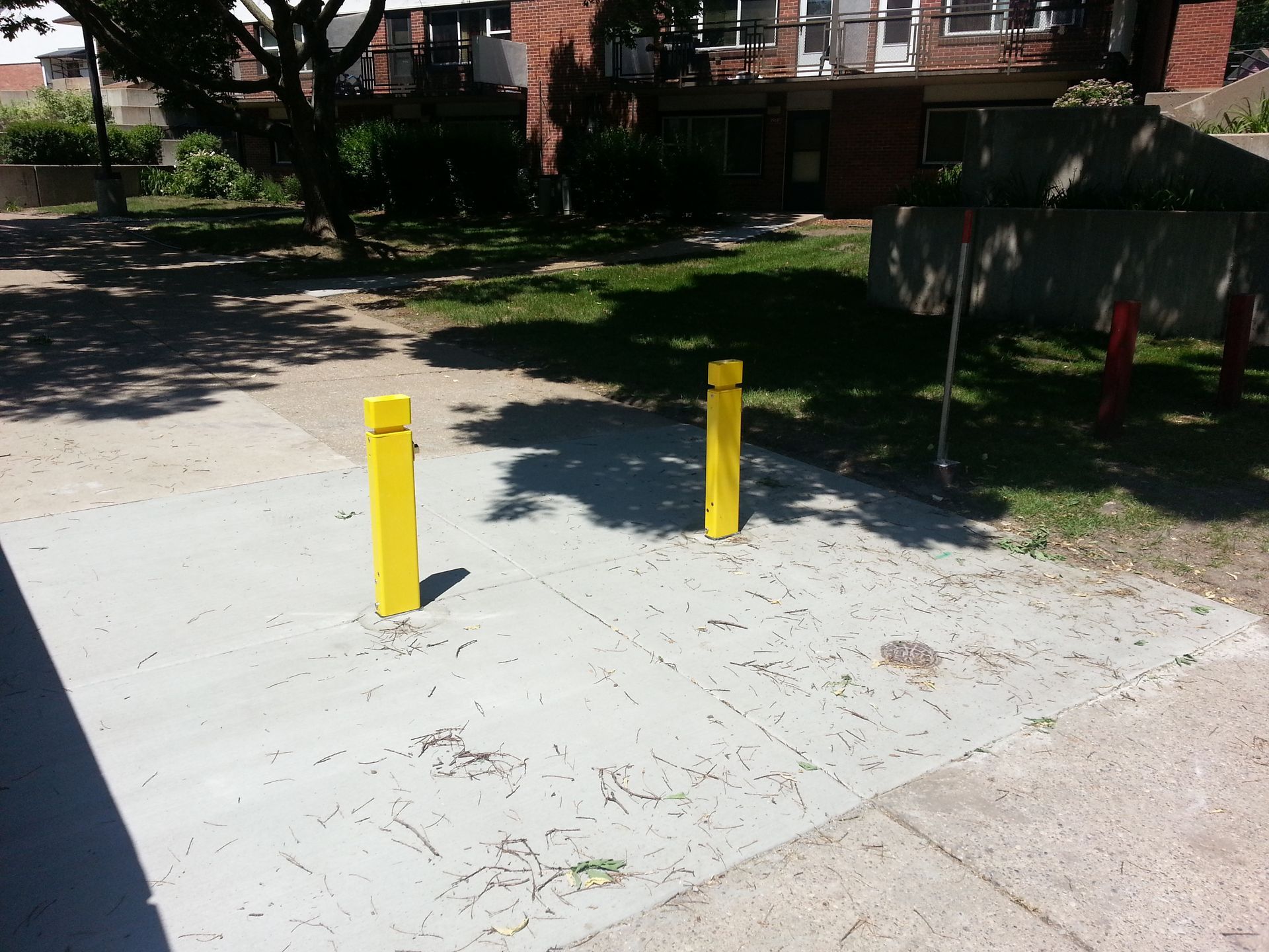 Two yellow bollards on a concrete driveway near trees and apartment buildings