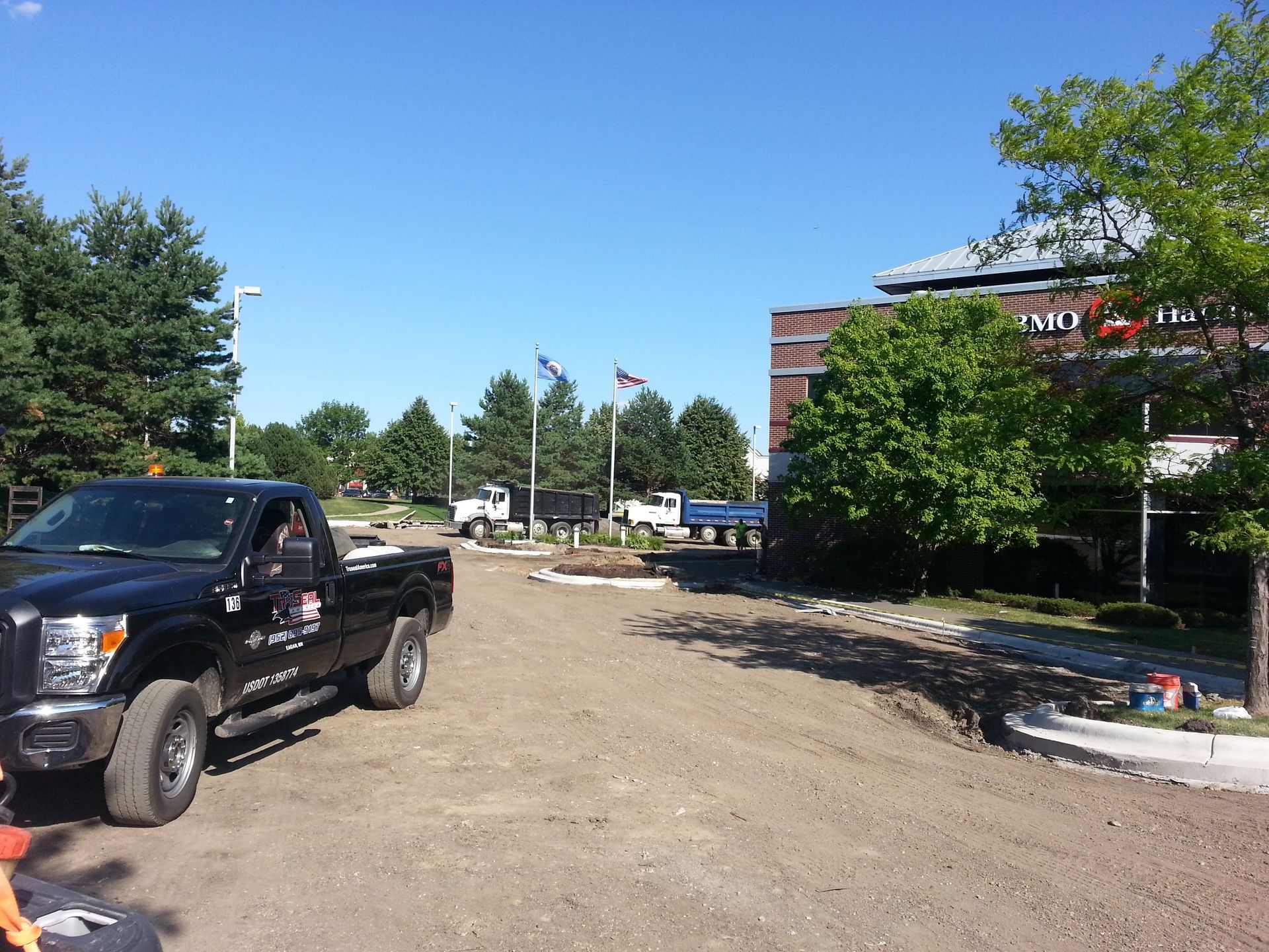 Black pickup truck on a dirt lot near trees and a building under a clear blue sky