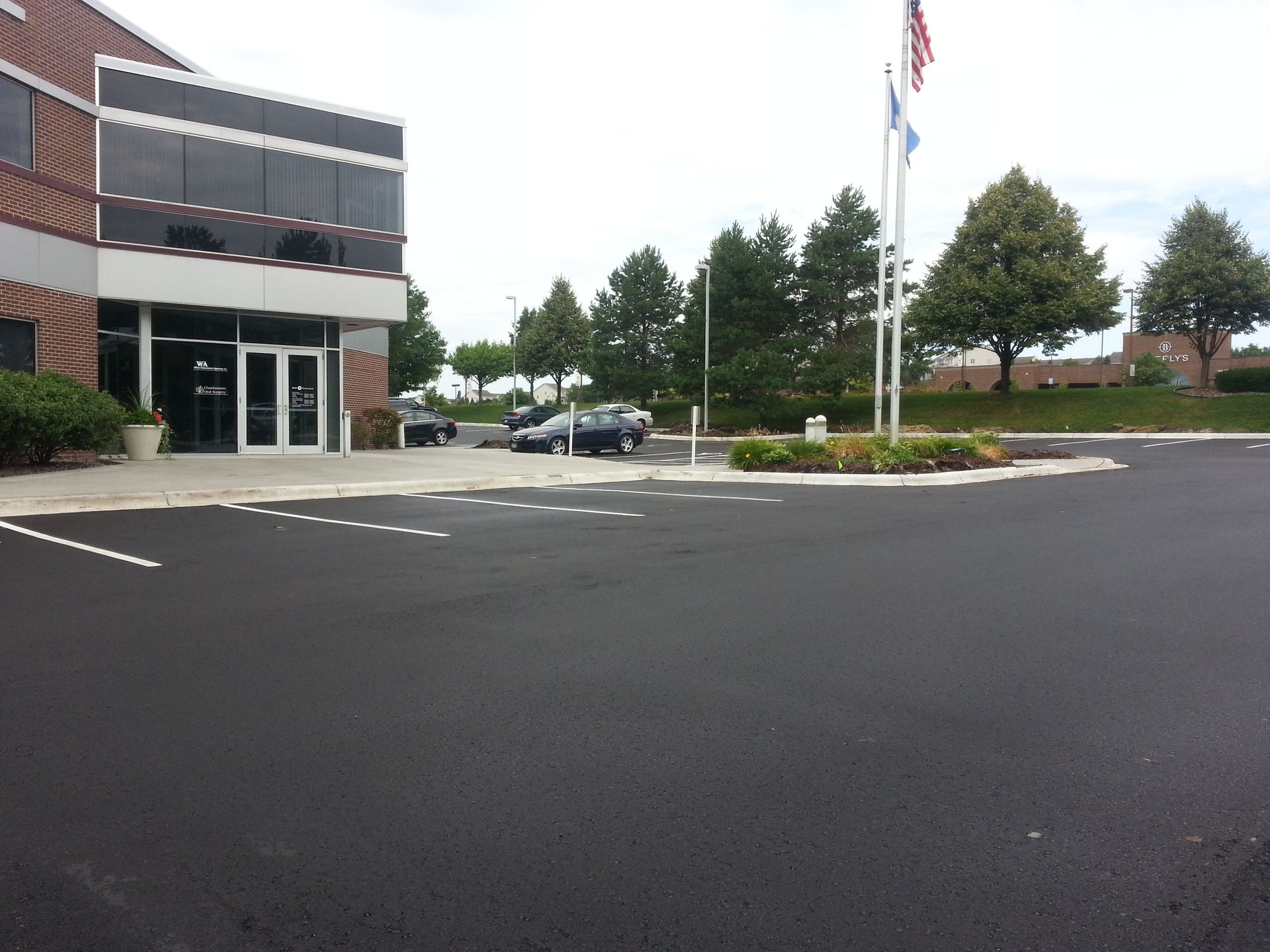 Office building with parking lot, trees, and flagpoles on an overcast day