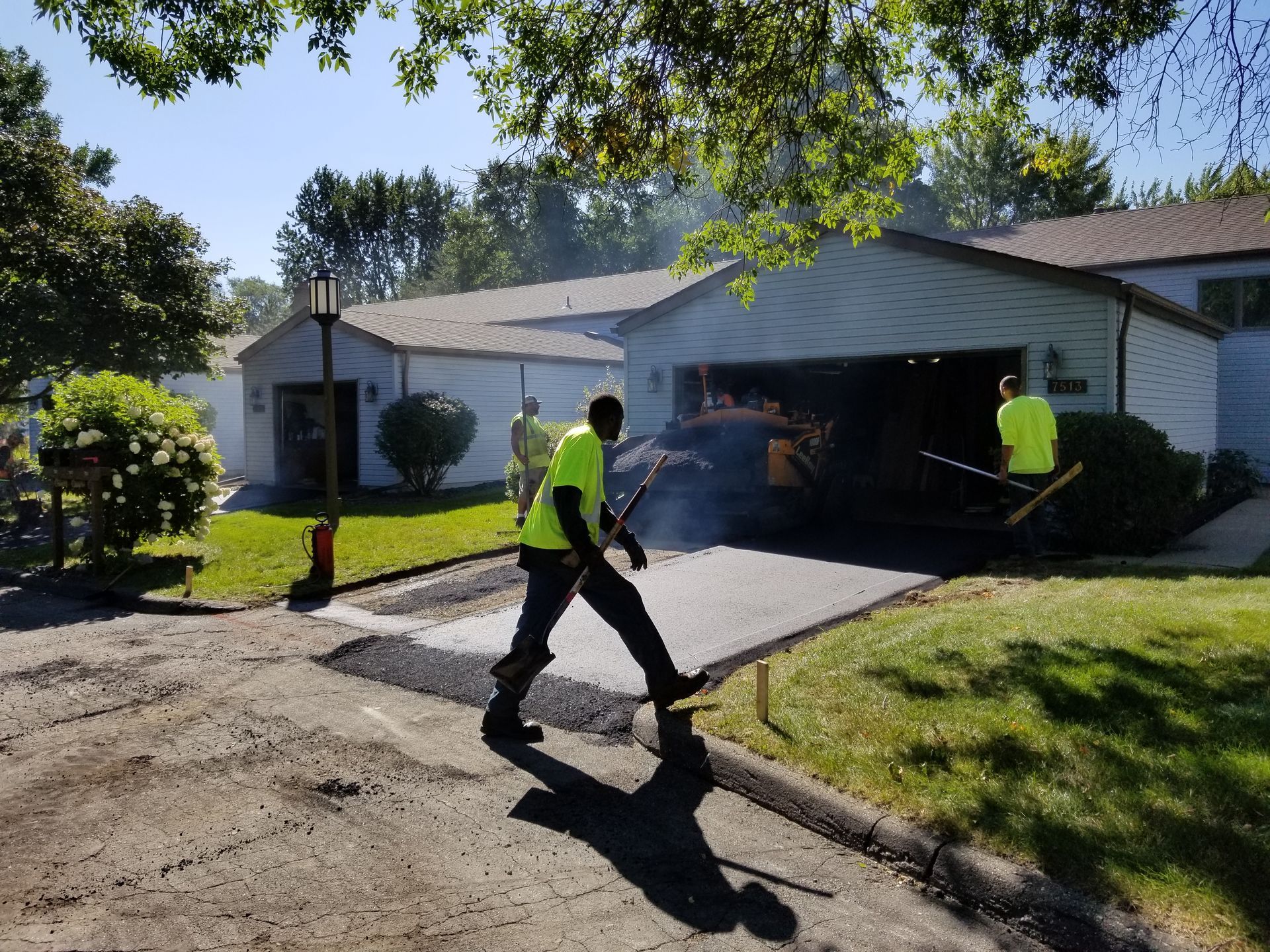 Workers in neon shirts spraying a house roof, with smoke or mist over the driveway