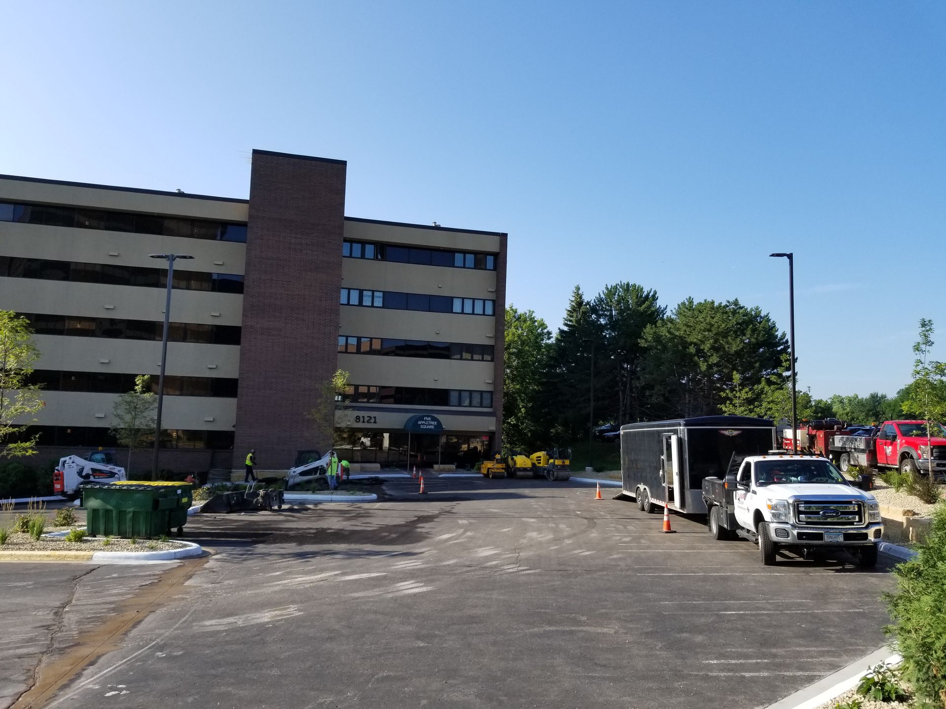 Apartment building parking lot with trucks and construction equipment under a clear blue sky