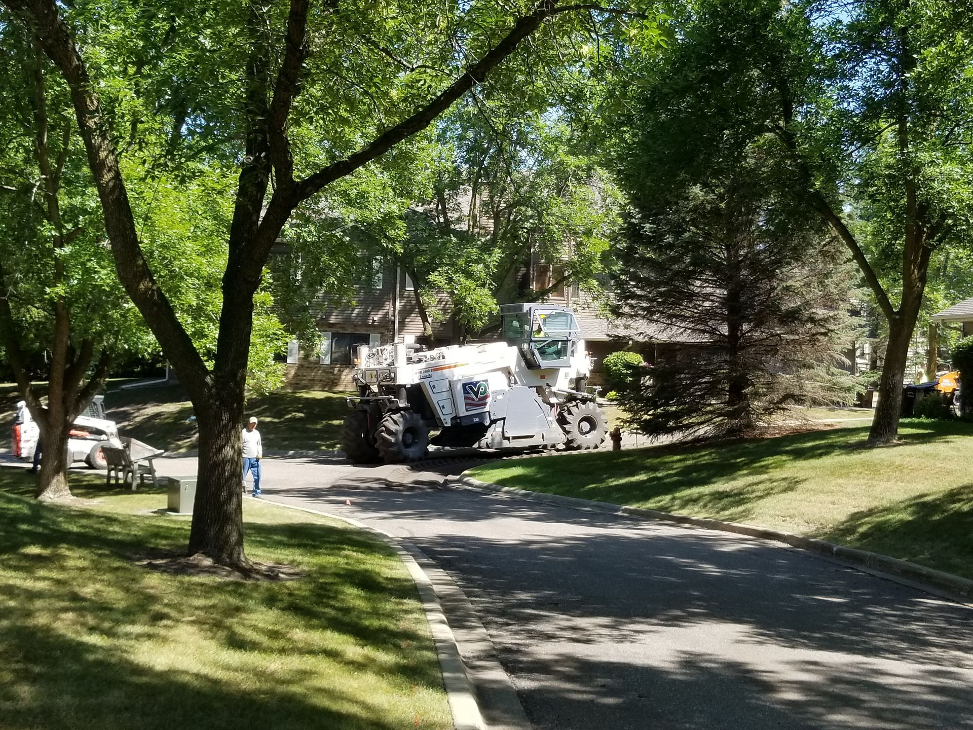 Tree-lined suburban street with a white utility truck parked near houses on a sunny day