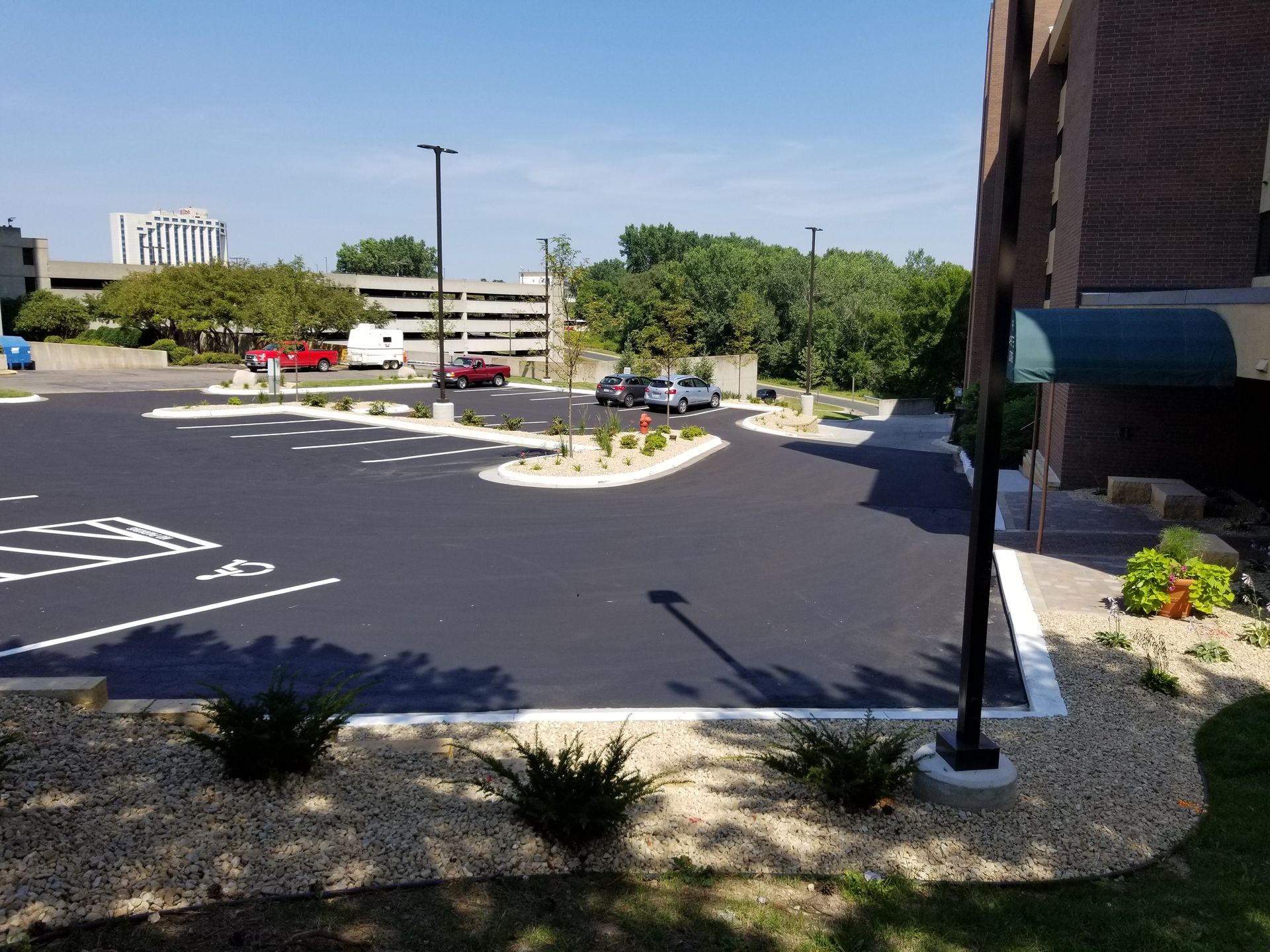 Parking lot with painted spaces, cars, and a brick building under a sunny sky