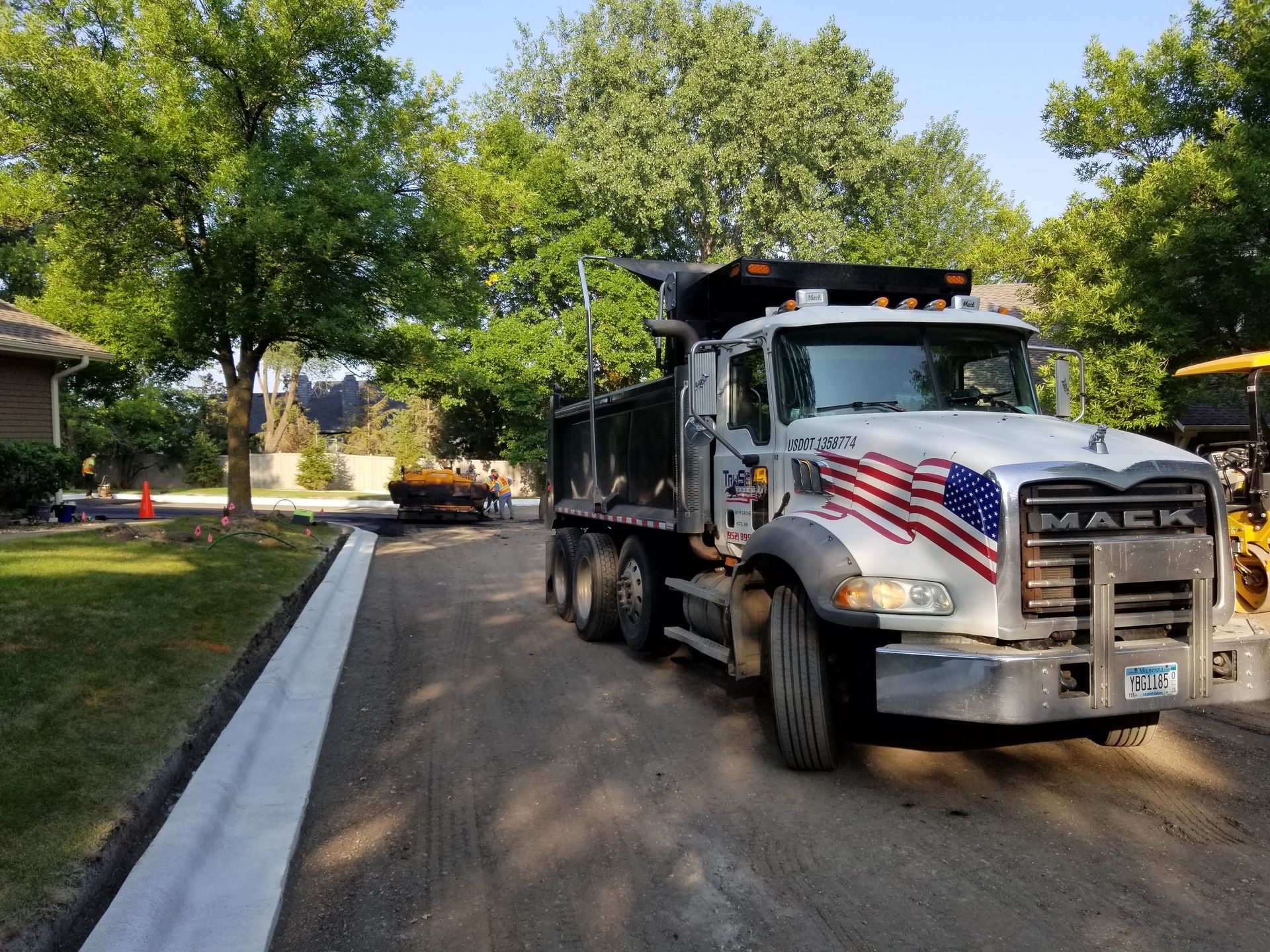 White dump truck parked on a tree-lined residential street beside a curb and sidewalk