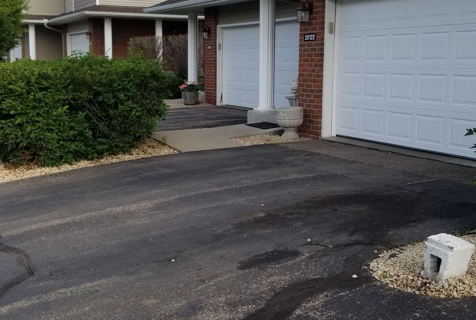 Driveway and garage entrance of a brick townhouse with shrubs and two white garage doors