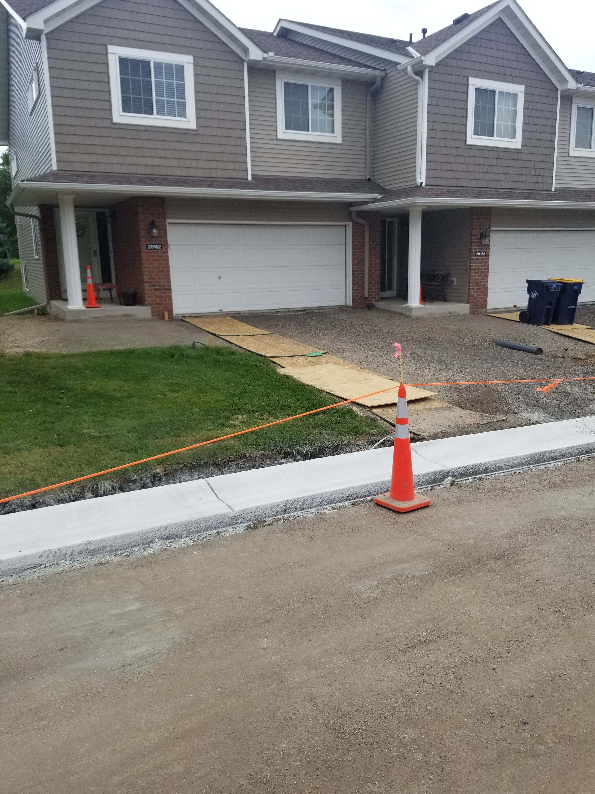 New townhouses with garages beside a dirt road and orange construction cones at the curb