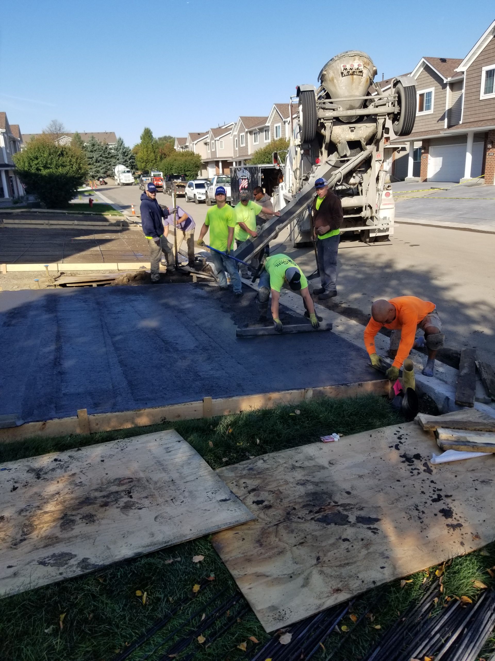 Workers pouring concrete driveway beside a cement truck in a suburban neighborhood