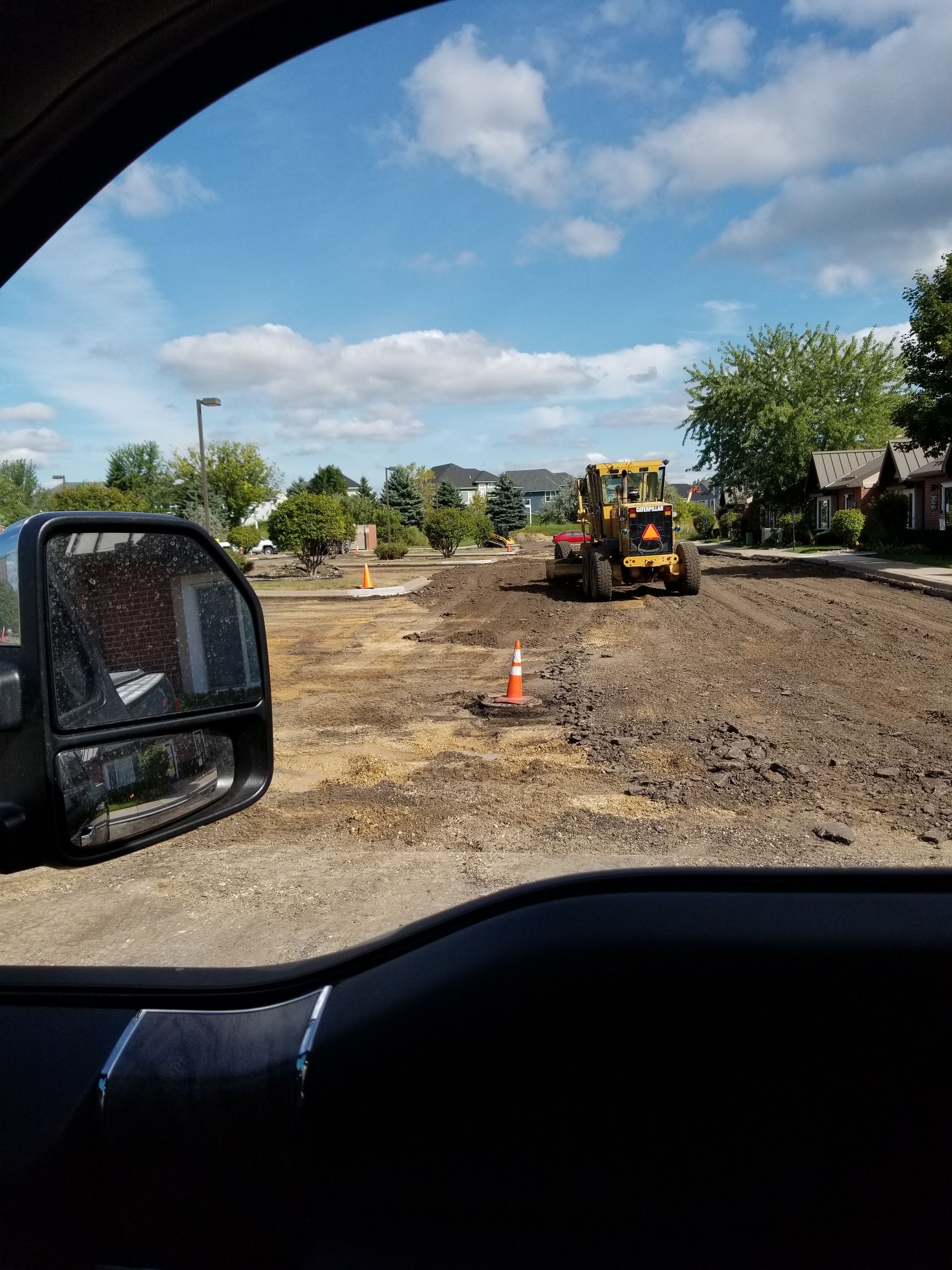 Roadwork scene with a yellow construction loader on a dirt road under a partly cloudy sky.