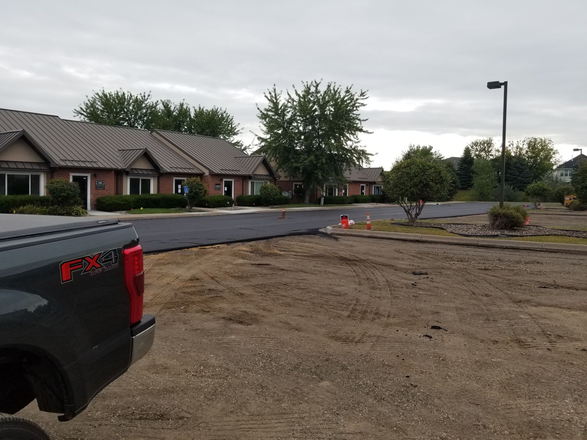 Residential street with brick houses, overcast sky, and a truck parked beside a dirt lot