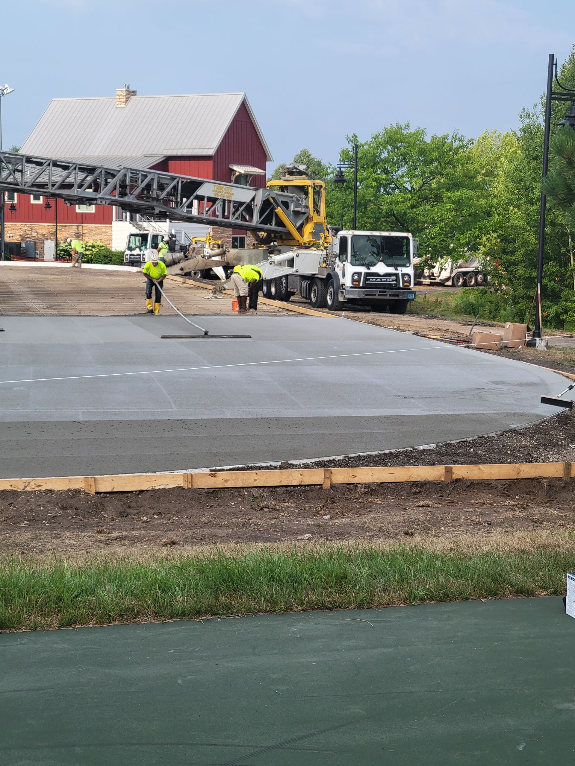 Road construction site with workers, crane truck, and a new concrete slab beside a house