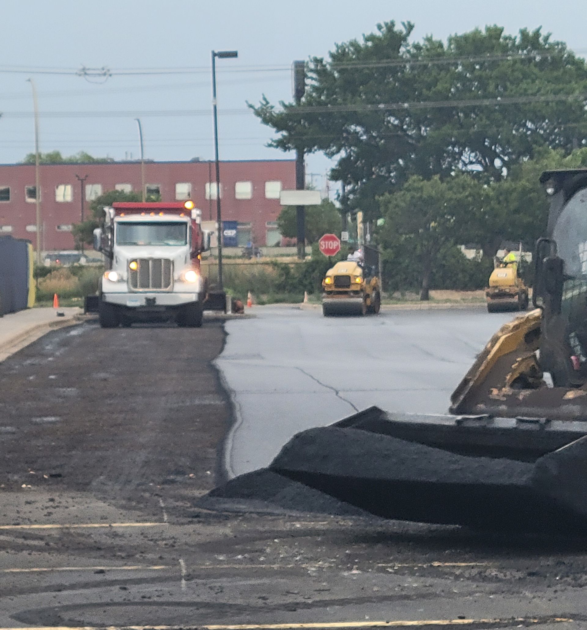 Road construction with heavy equipment paving a street near a red-brick building.