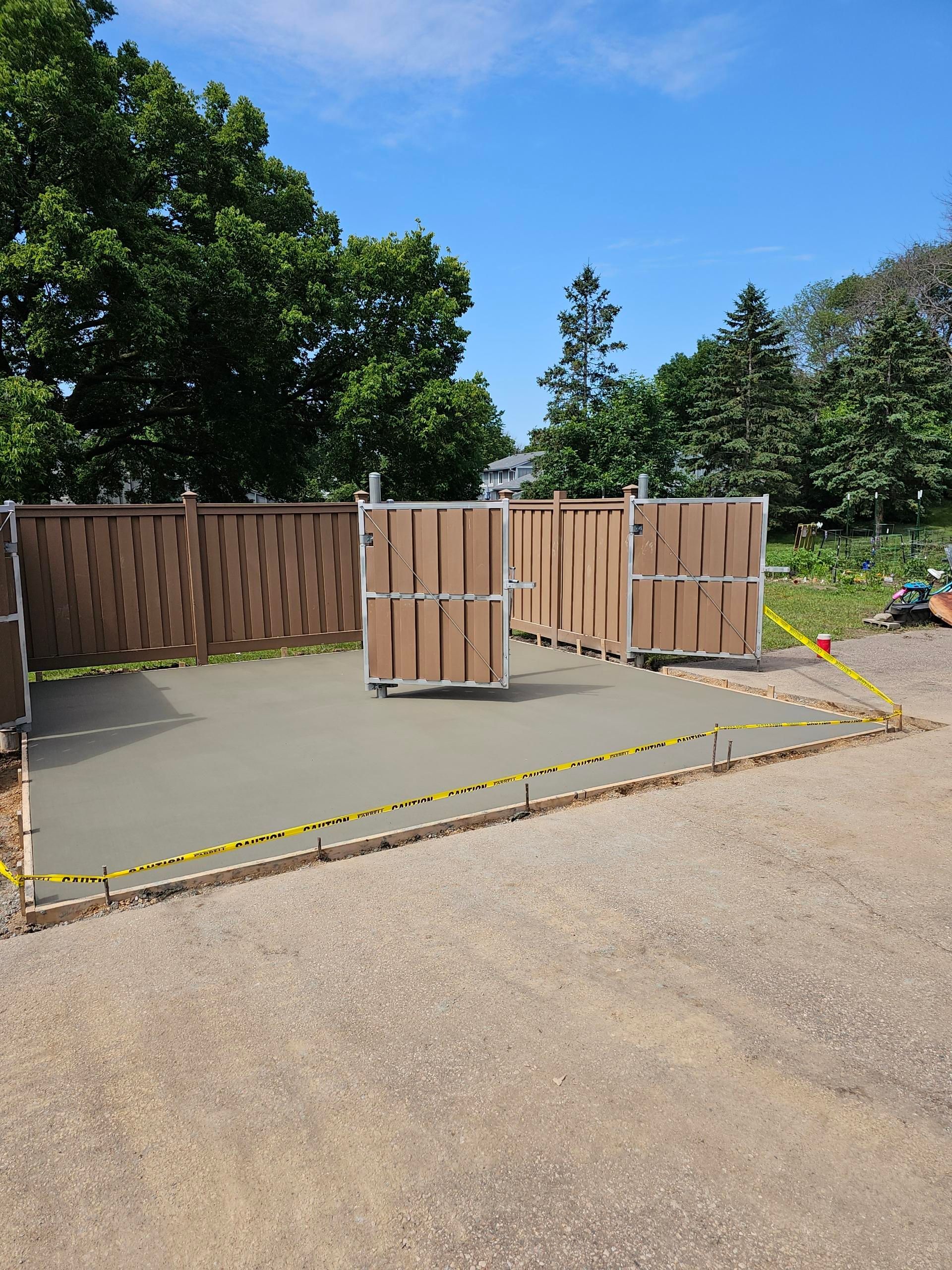 Empty fenced outdoor area with a wooden gate and caution tape beside a gravel path under a blue sky