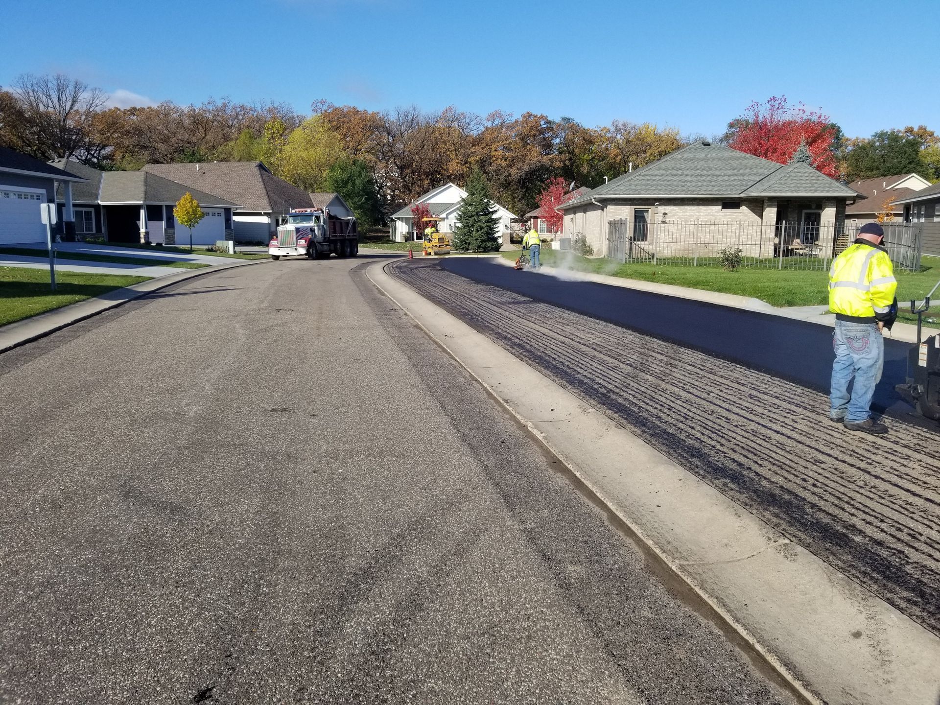 Road resurfacing on a suburban street, with a worker in a reflective jacket beside fresh asphalt.