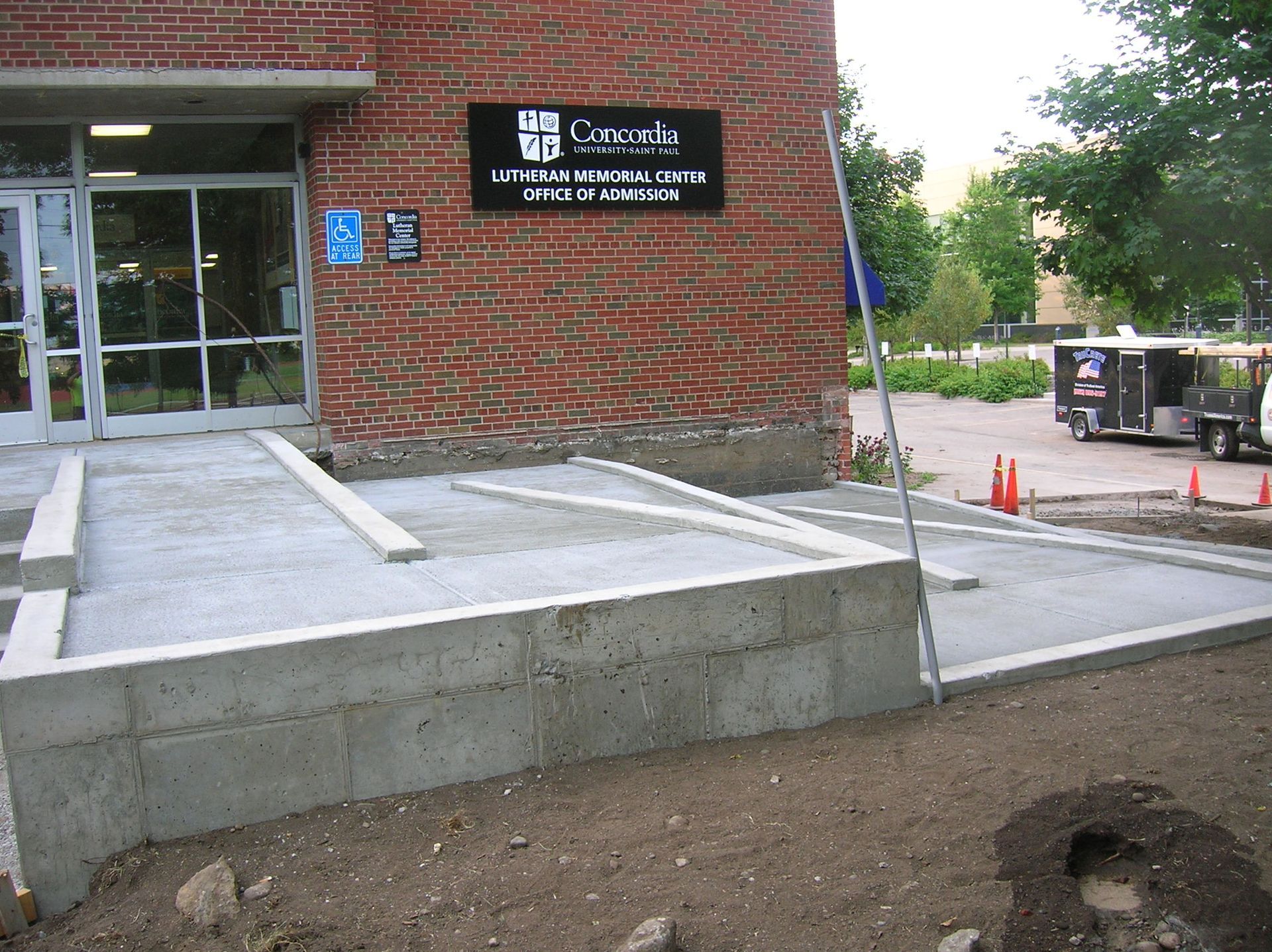 Brick building entrance with wheelchair ramp and sign reading “Council Library,” beside a dirt path.