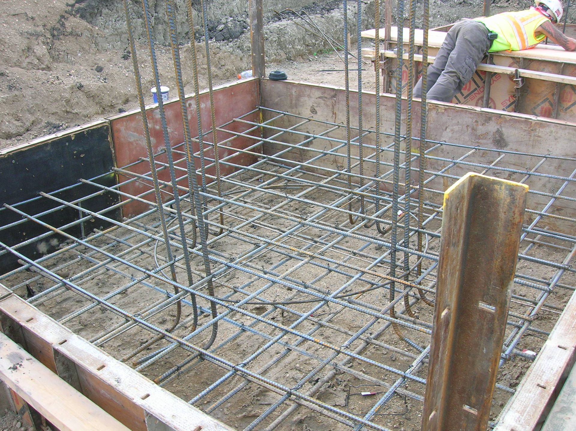 Rebar grid in a concrete foundation pit, with a worker kneeling at the edge