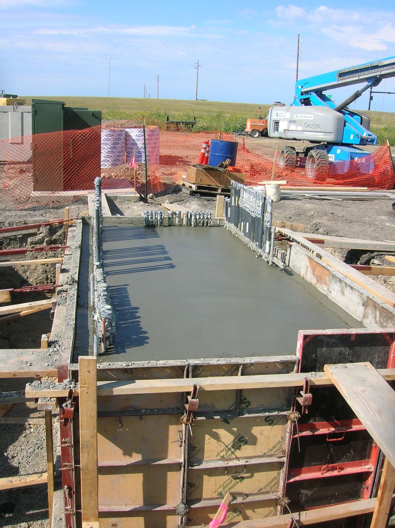 Concrete foundation being poured at a construction site, with rebar, formwork, and machinery in the background.