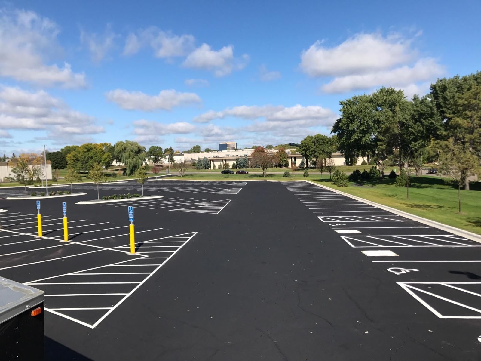 Empty parking lot with painted spaces, yellow bollards, and trees under a blue sky