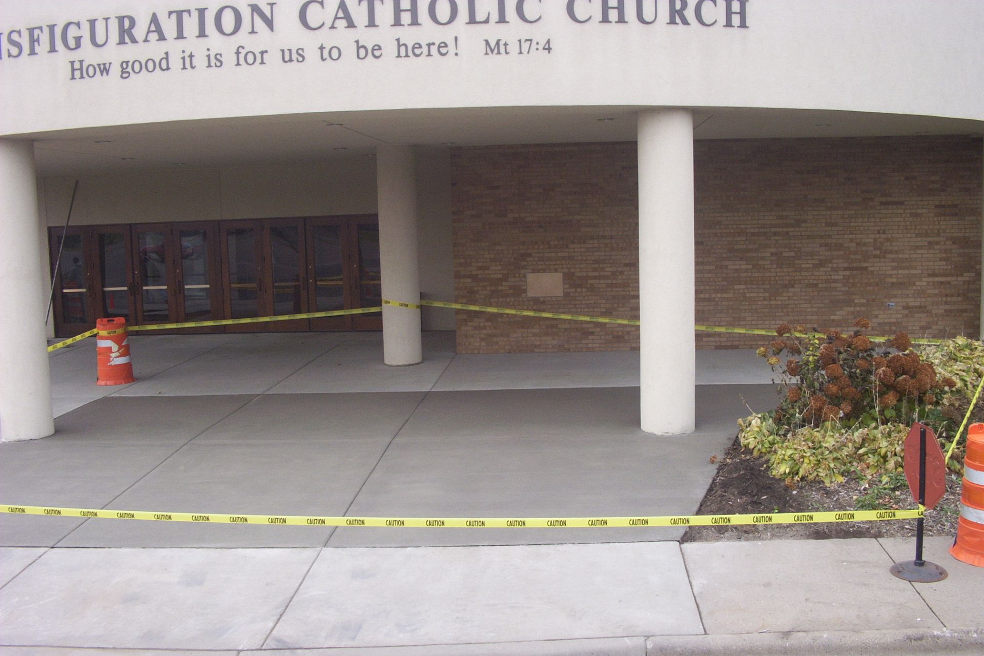 Caution-taped church entrance with columns, closed doors, and orange cones under a covered walkway