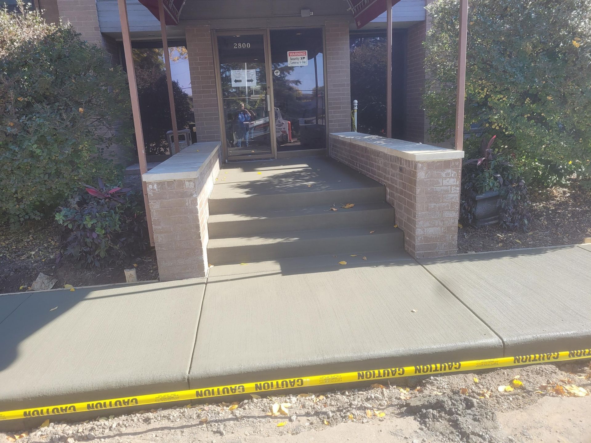 Building entrance with steps and brick railings, bordered by yellow caution tape along the sidewalk.