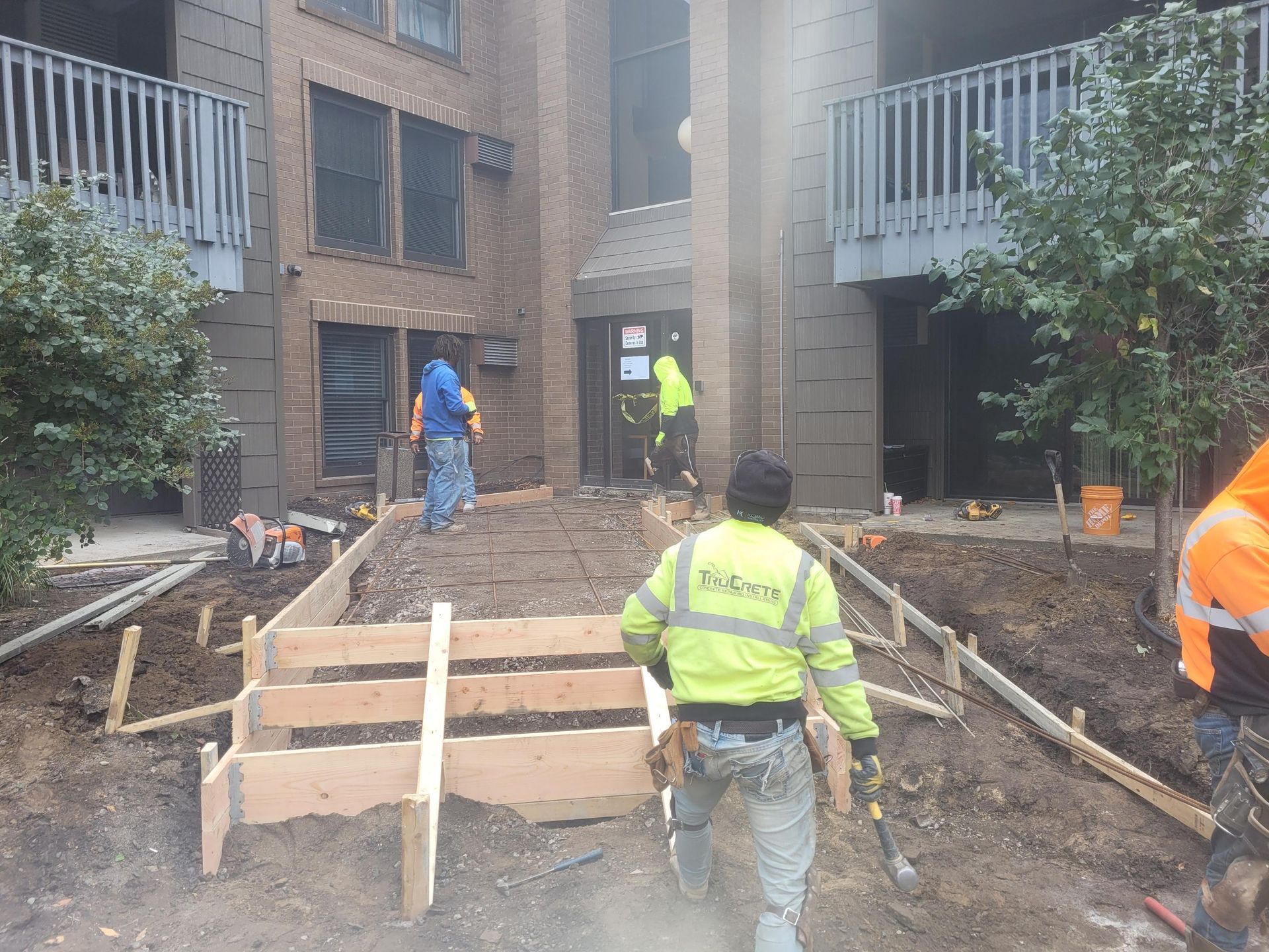 Construction workers pouring concrete on a walkway between brick apartment buildings.