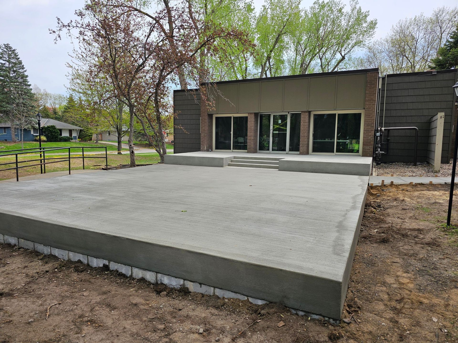 Concrete patio slab in front of a modern building with glass doors and trees nearby