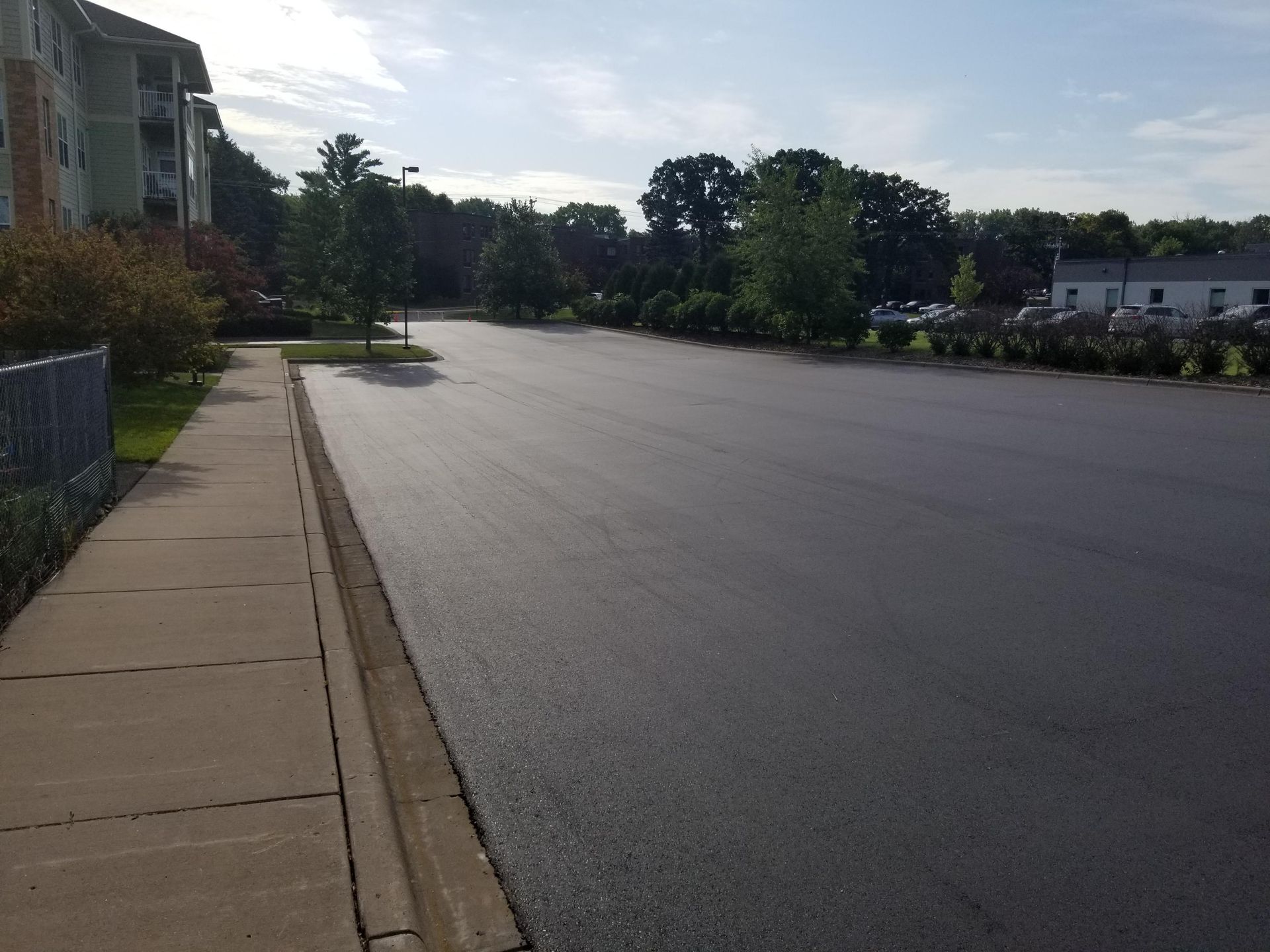 Empty suburban street beside a sidewalk, trees, and apartment buildings on a sunny day