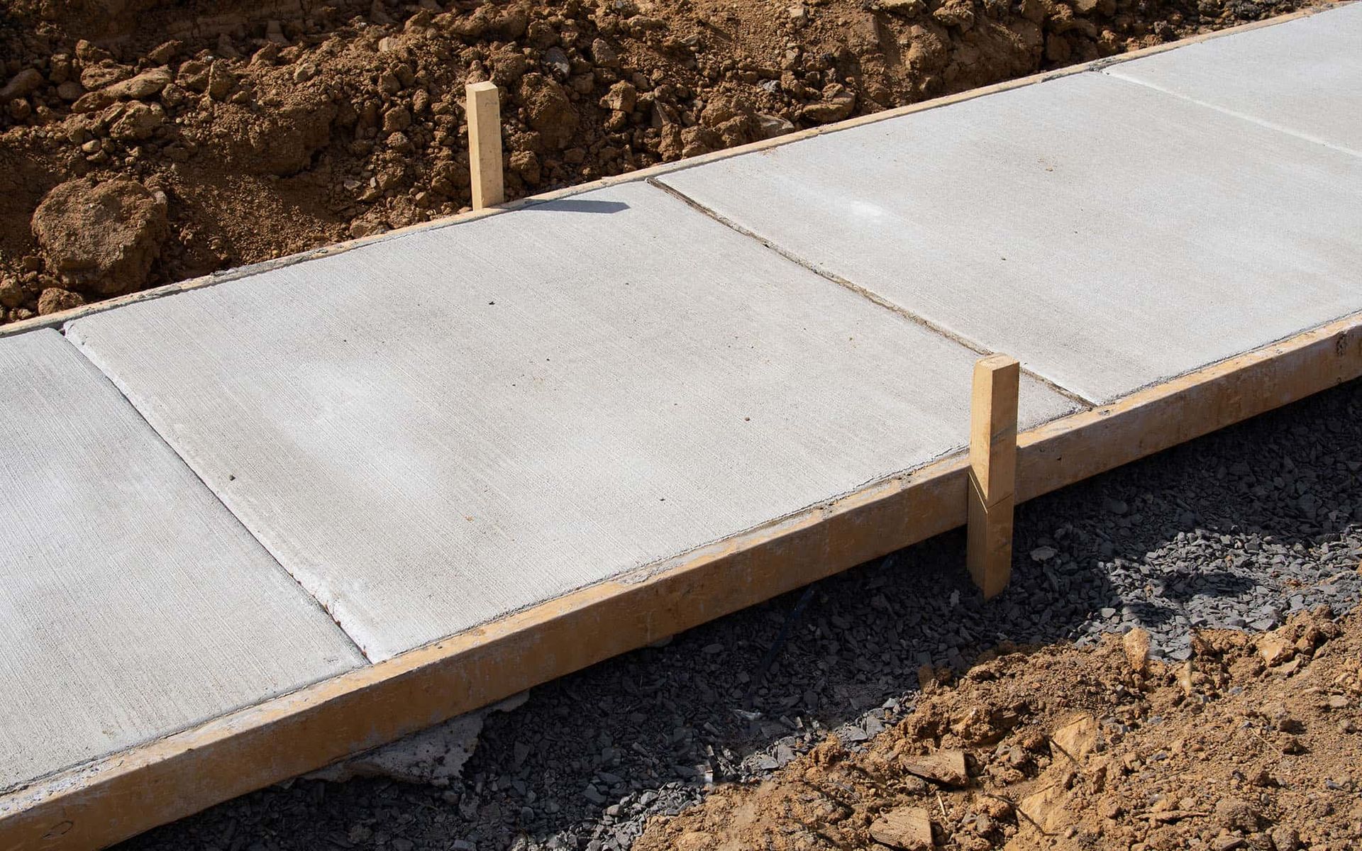 Fresh concrete sidewalk slabs being set with wooden forms at a construction site.