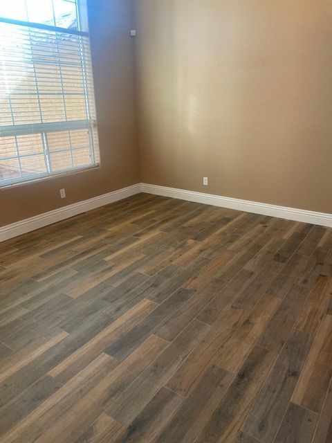 Empty room with wood-look flooring, beige walls, white baseboards, and a window with blinds.