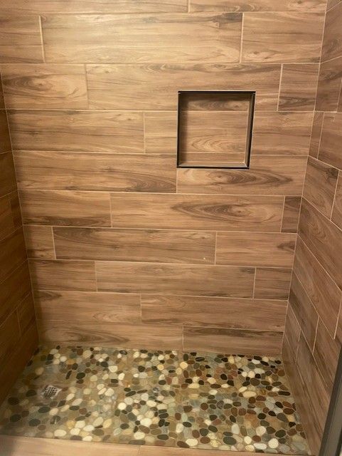 Shower with wood-look tiles and a pebble floor, a recessed shelf.