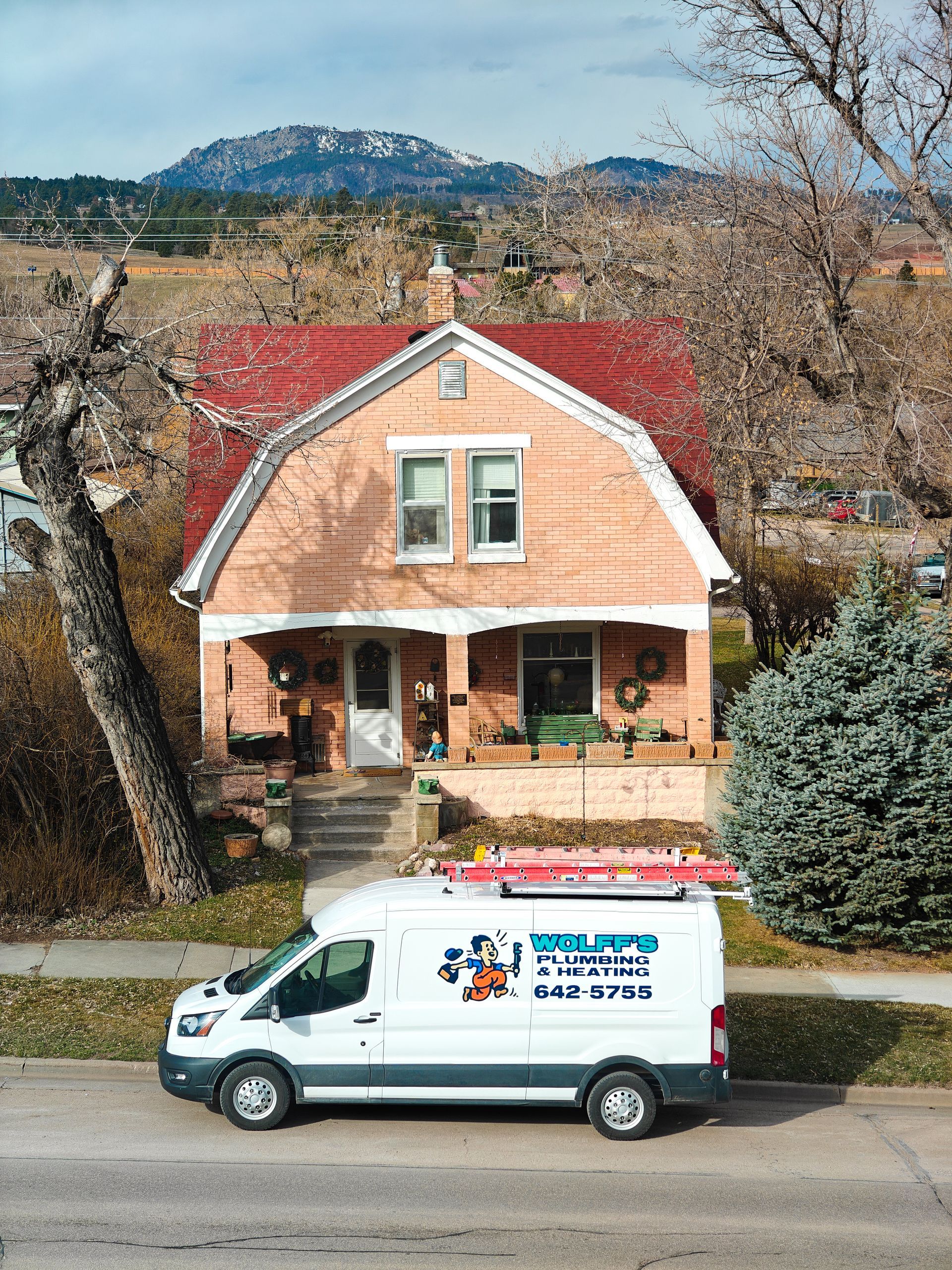 White service van parked in front of a pink house with a red roof; a mountain is in the background.