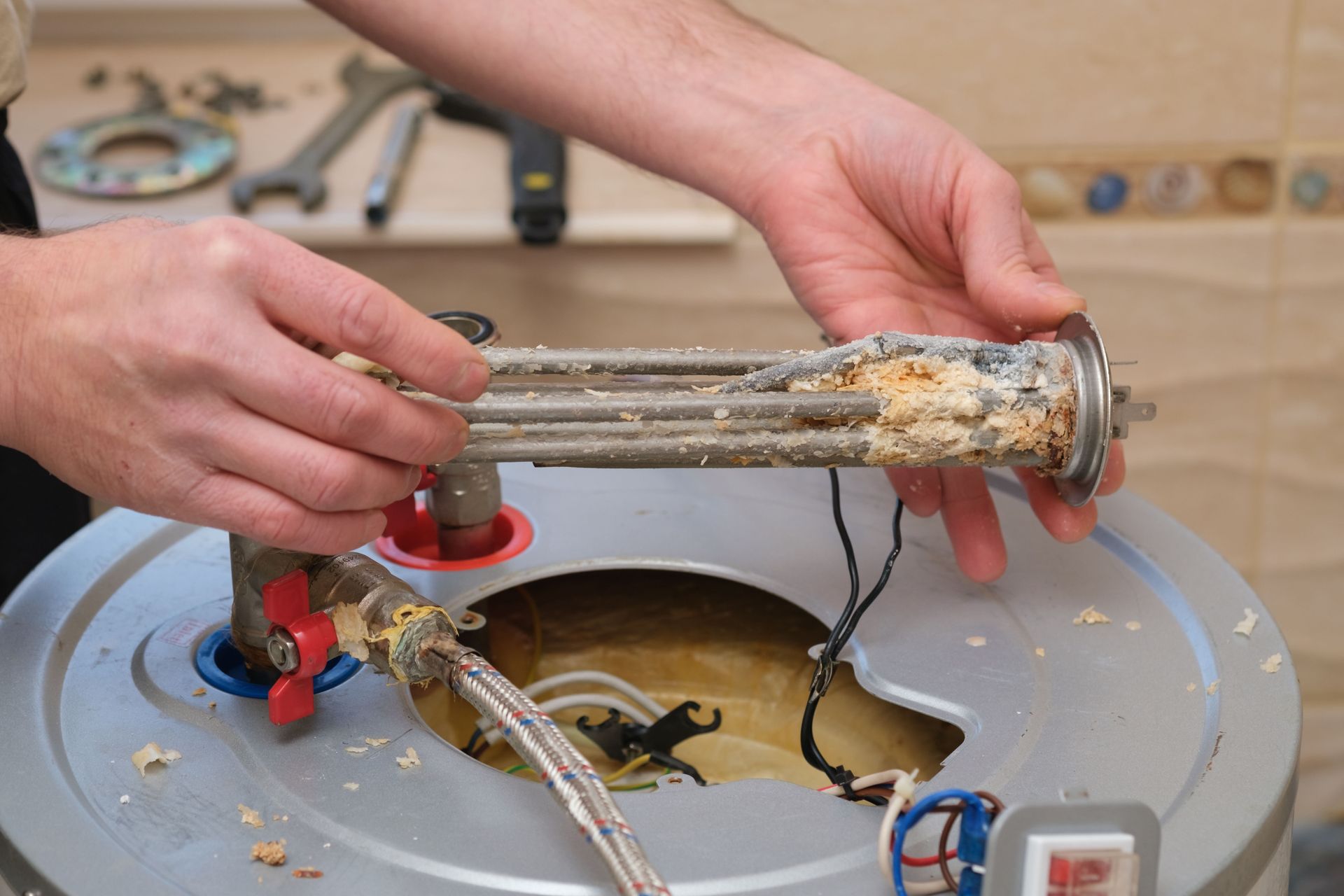 Hands cleaning a debris-clogged sink drain with tools and a hose under the counter