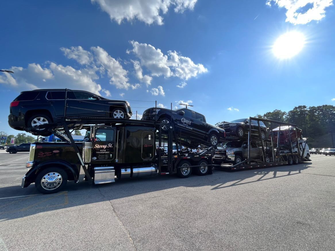 Car carrier truck loaded with black SUVs on a sunny highway under a blue sky.