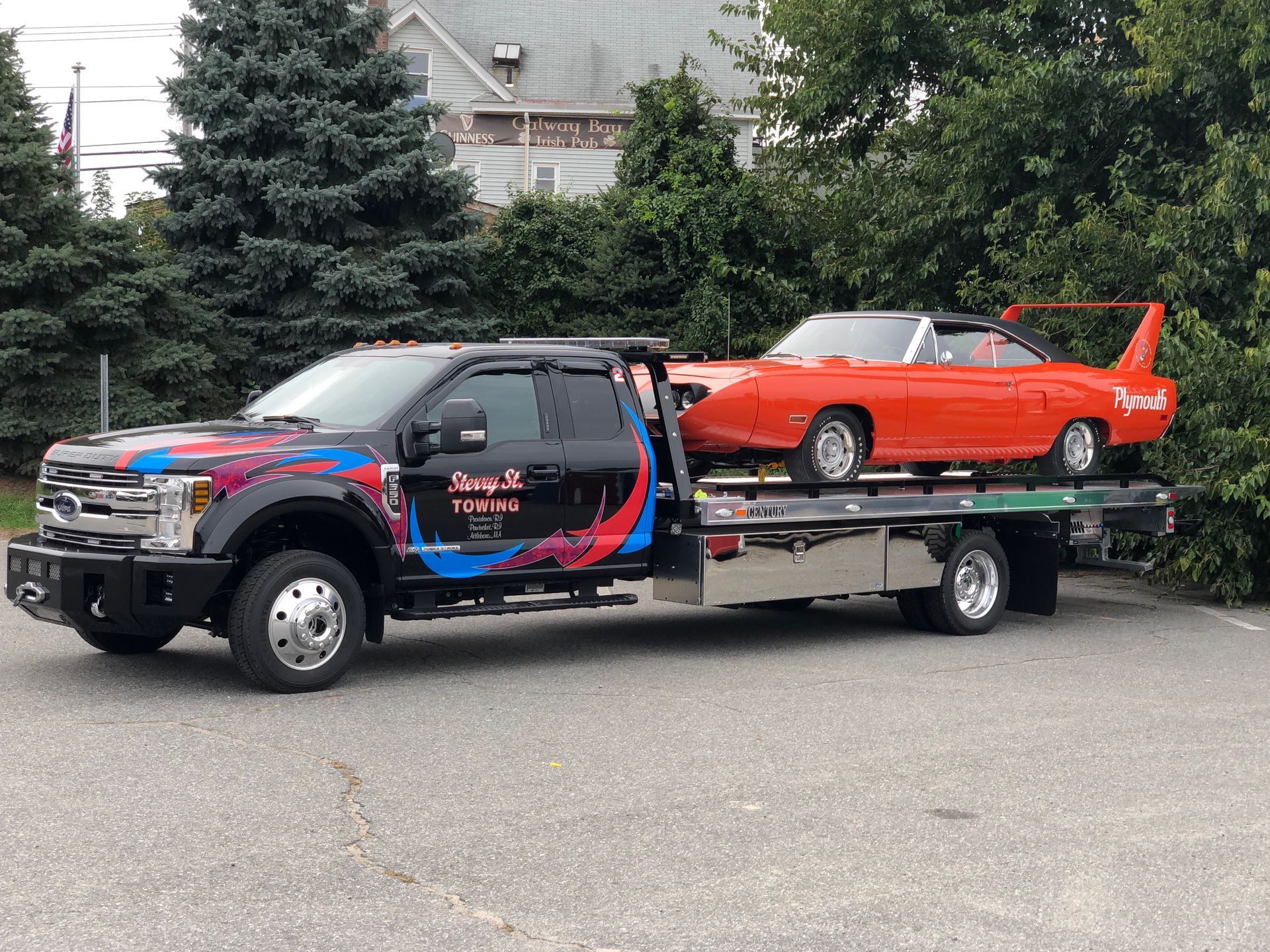 Custom black pickup towing a red vintage car on a flatbed trailer, parked outdoors.
