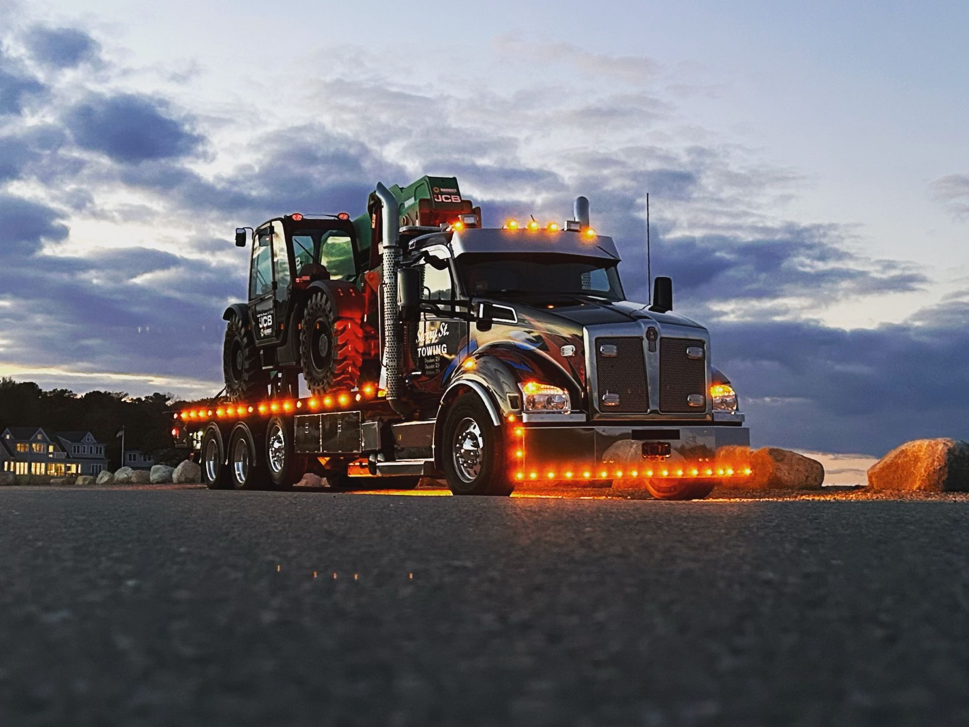 Custom-lit semi truck with glowing orange lights on a road at dusk under a cloudy sky.