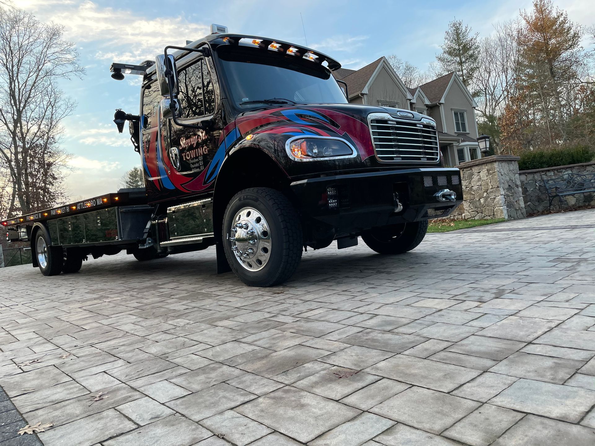 Black flatbed tow truck on a stone driveway, with blue and red graphics and chrome details.
