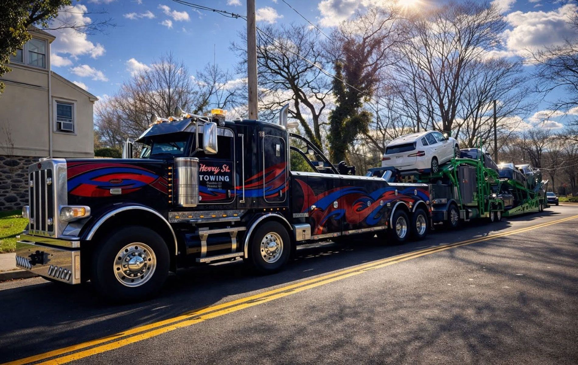 Two colorful tow trucks parked on a sunlit residential street with bare trees.
