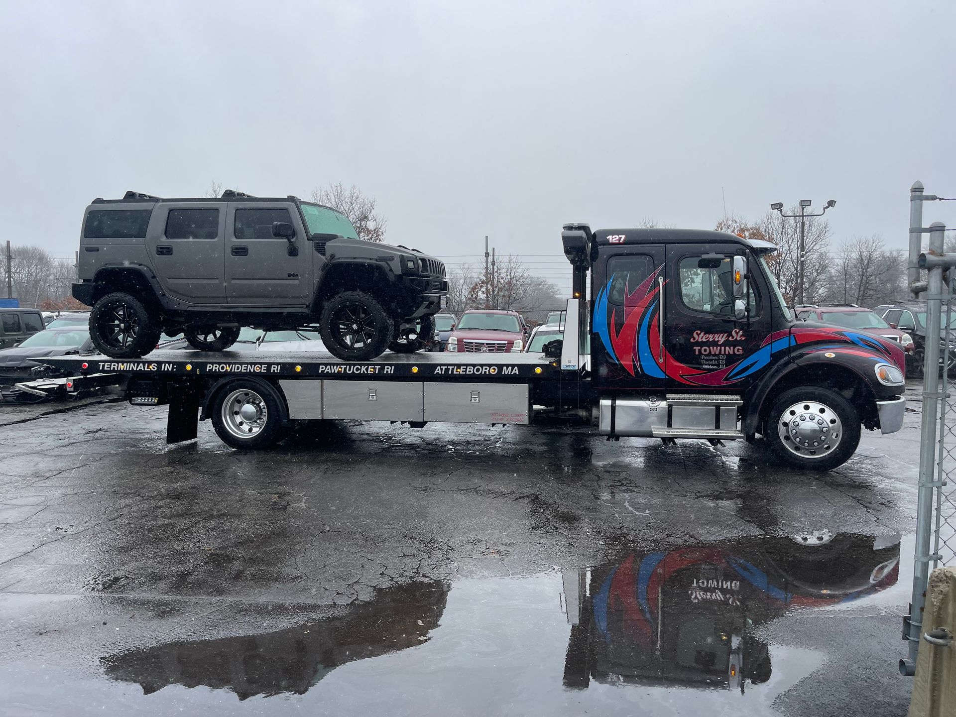 Flatbed tow truck carrying a gray SUV on a wet, snowy lot