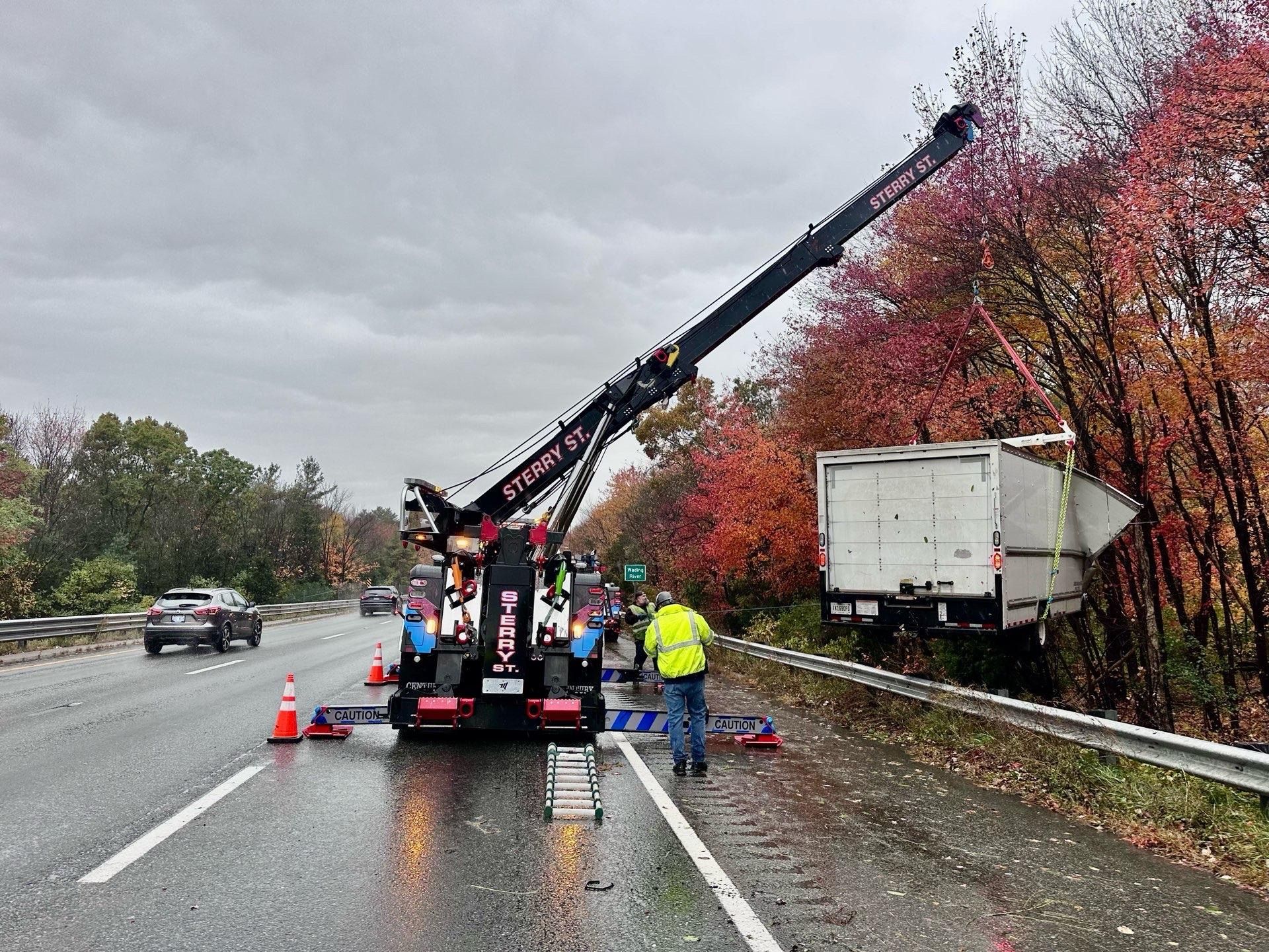 Roadside utility crew repairing power lines beside a highway, with a truck and cones under cloudy skies.