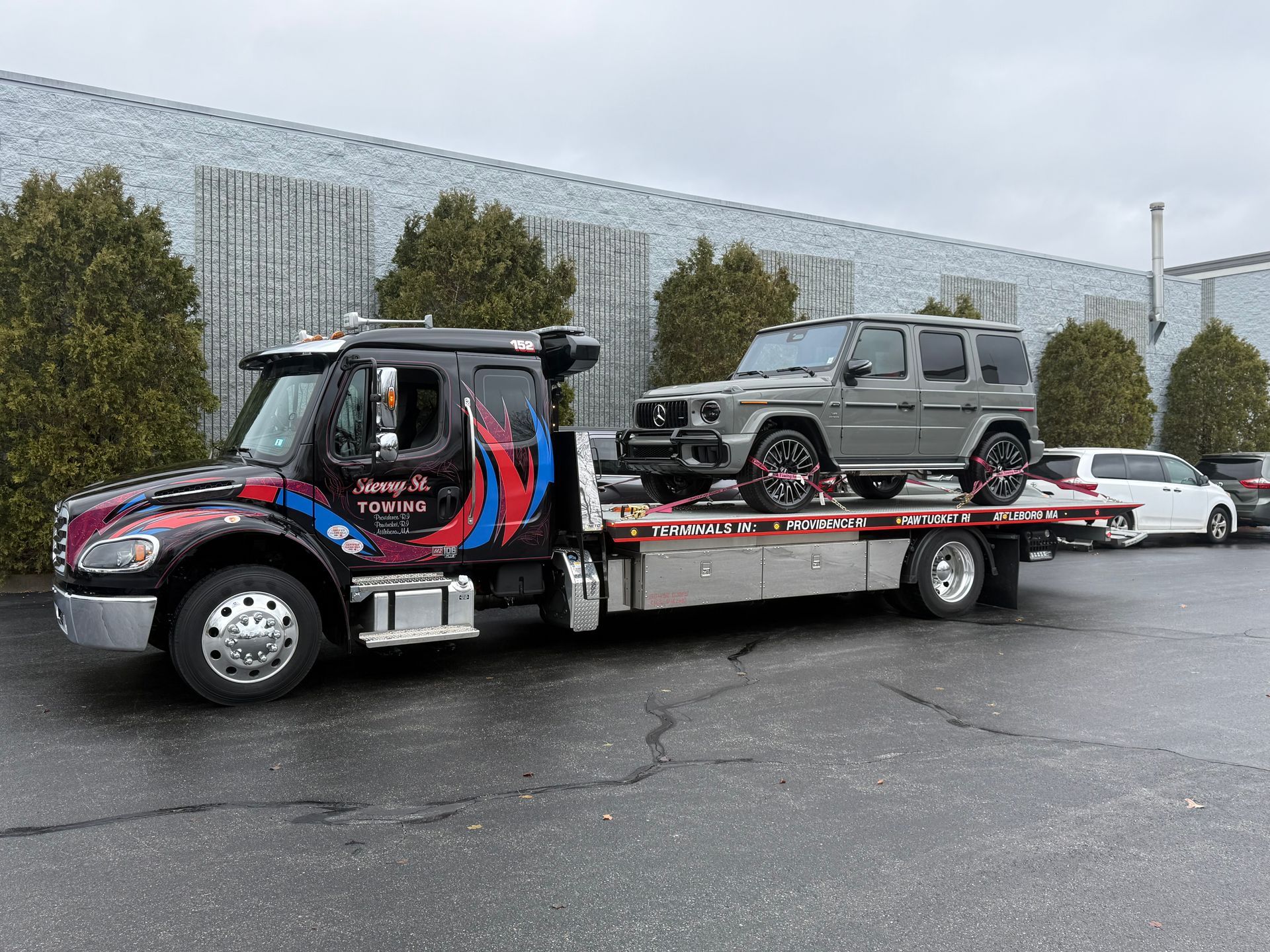 Tow truck hauling a gray off-road SUV on a flatbed in a parking lot.