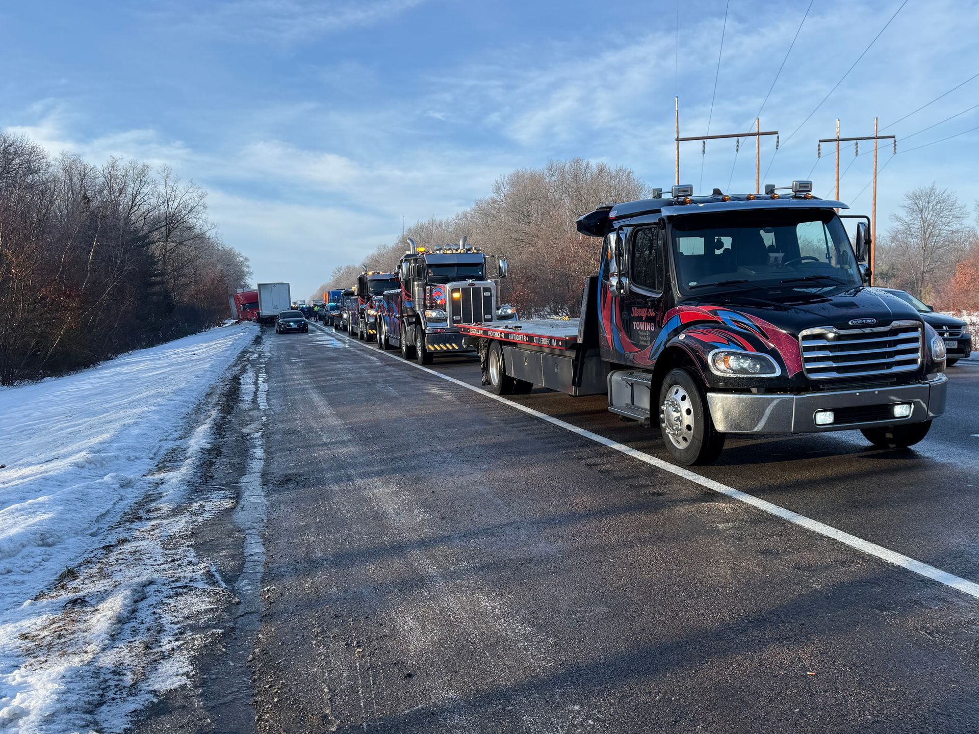 Tow truck hauling a car on a snowy roadside under a blue sky.