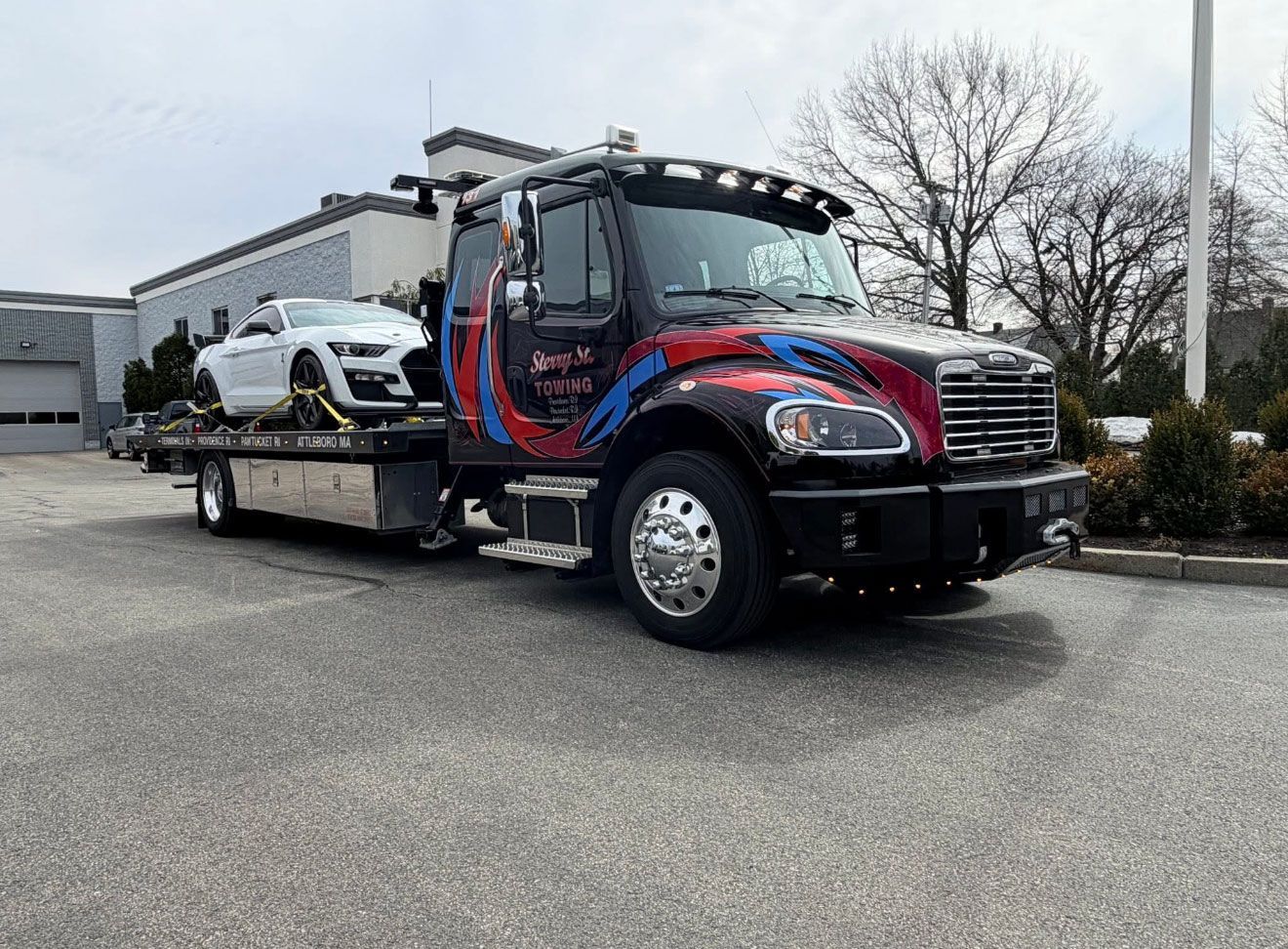 Tow truck carrying a white car in a parking lot, with a black and red cab.