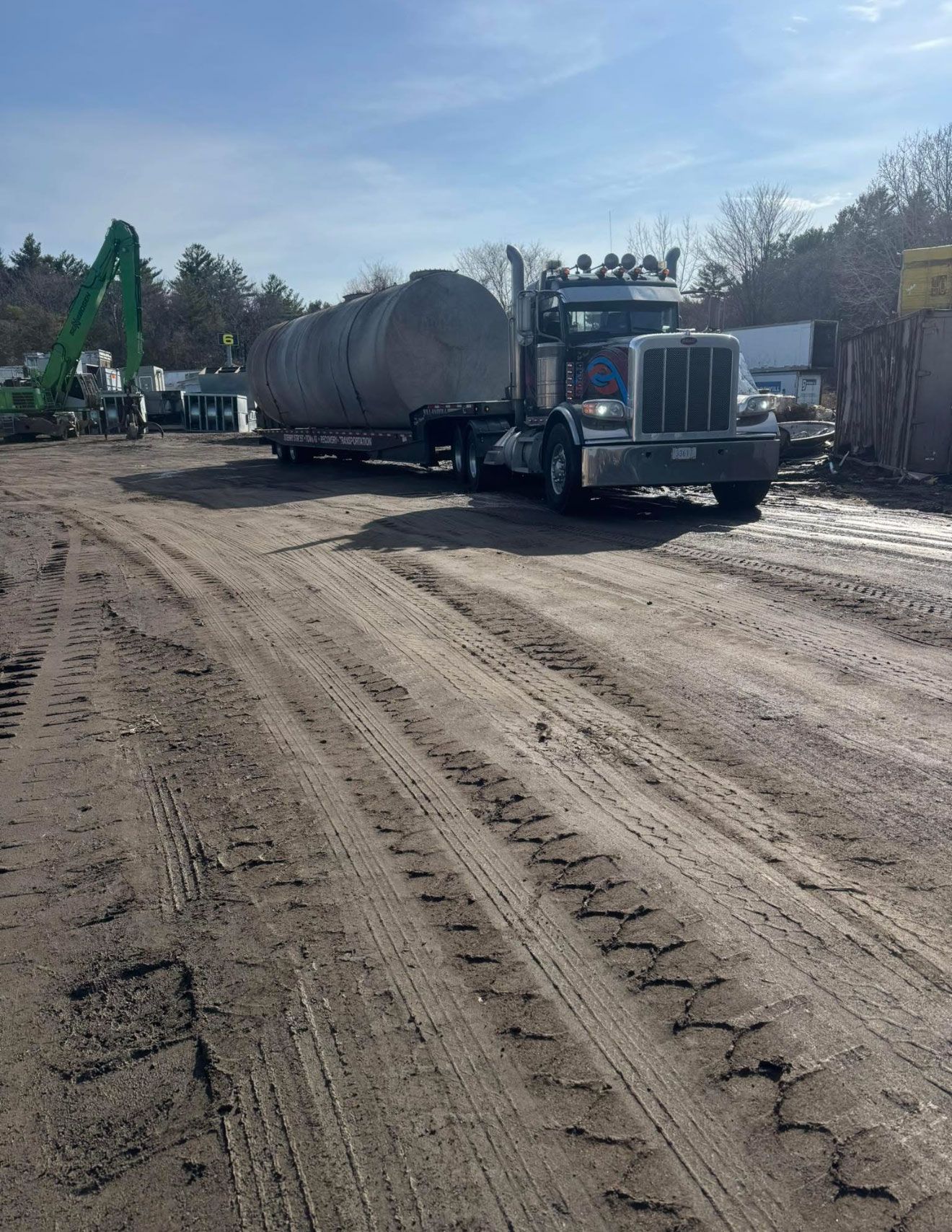 Semi-truck hauling a large cylindrical tank on a dirt road at a construction site.