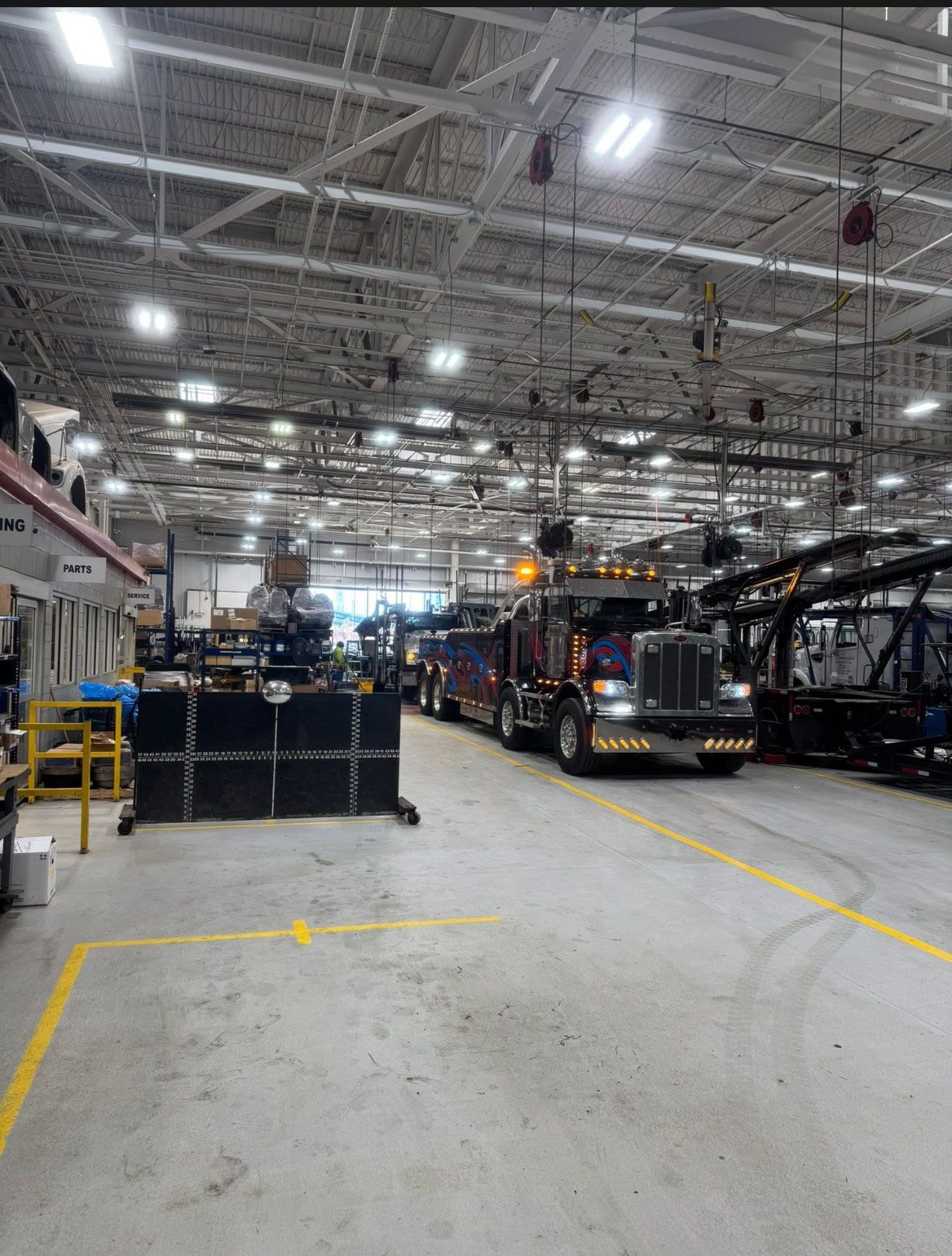 Inside a large warehouse, two utility trucks sit beneath bright overhead lights along a marked aisle.