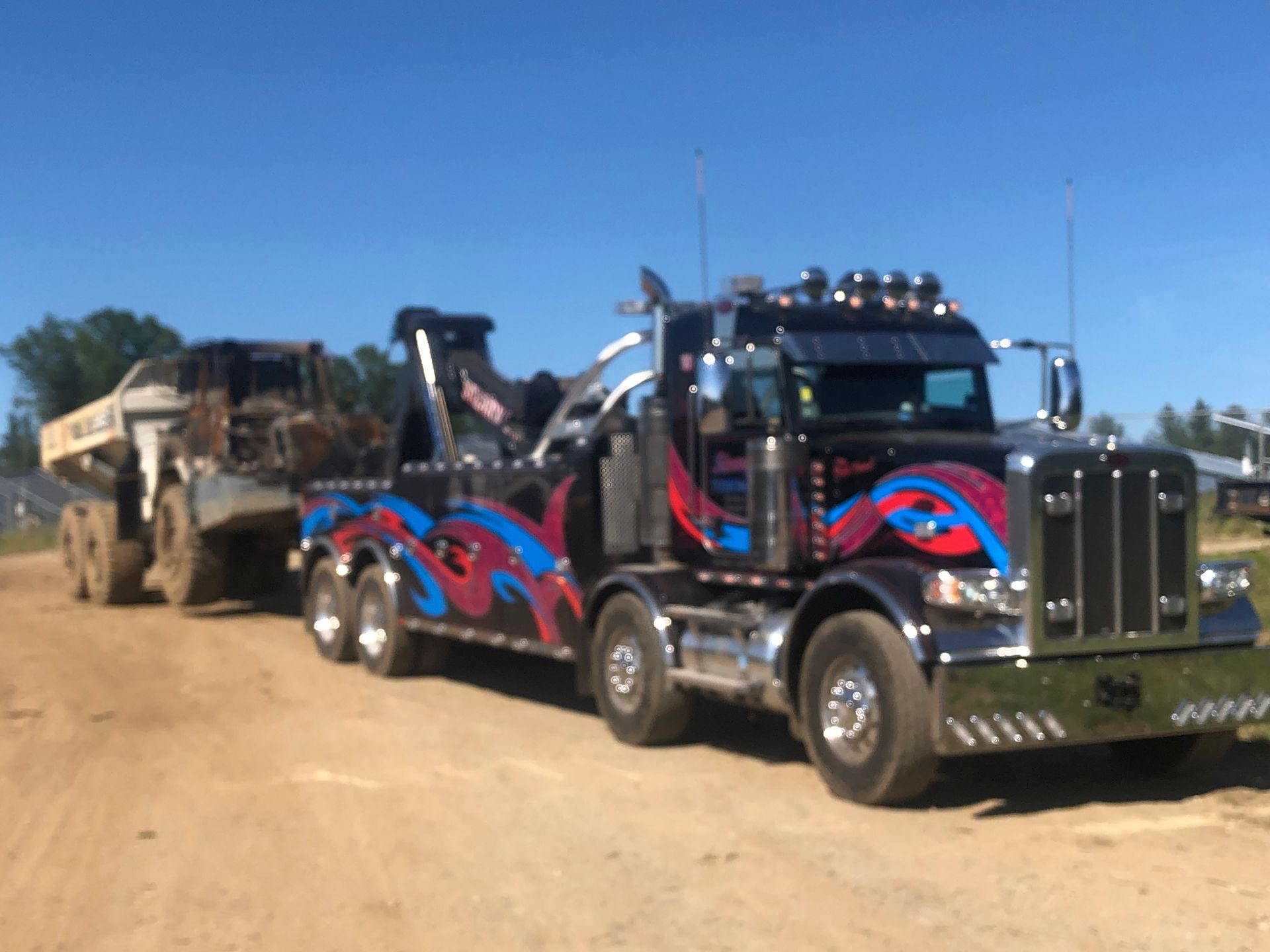 Black tow truck hauling a large dump truck on a dirt road under a clear blue sky.