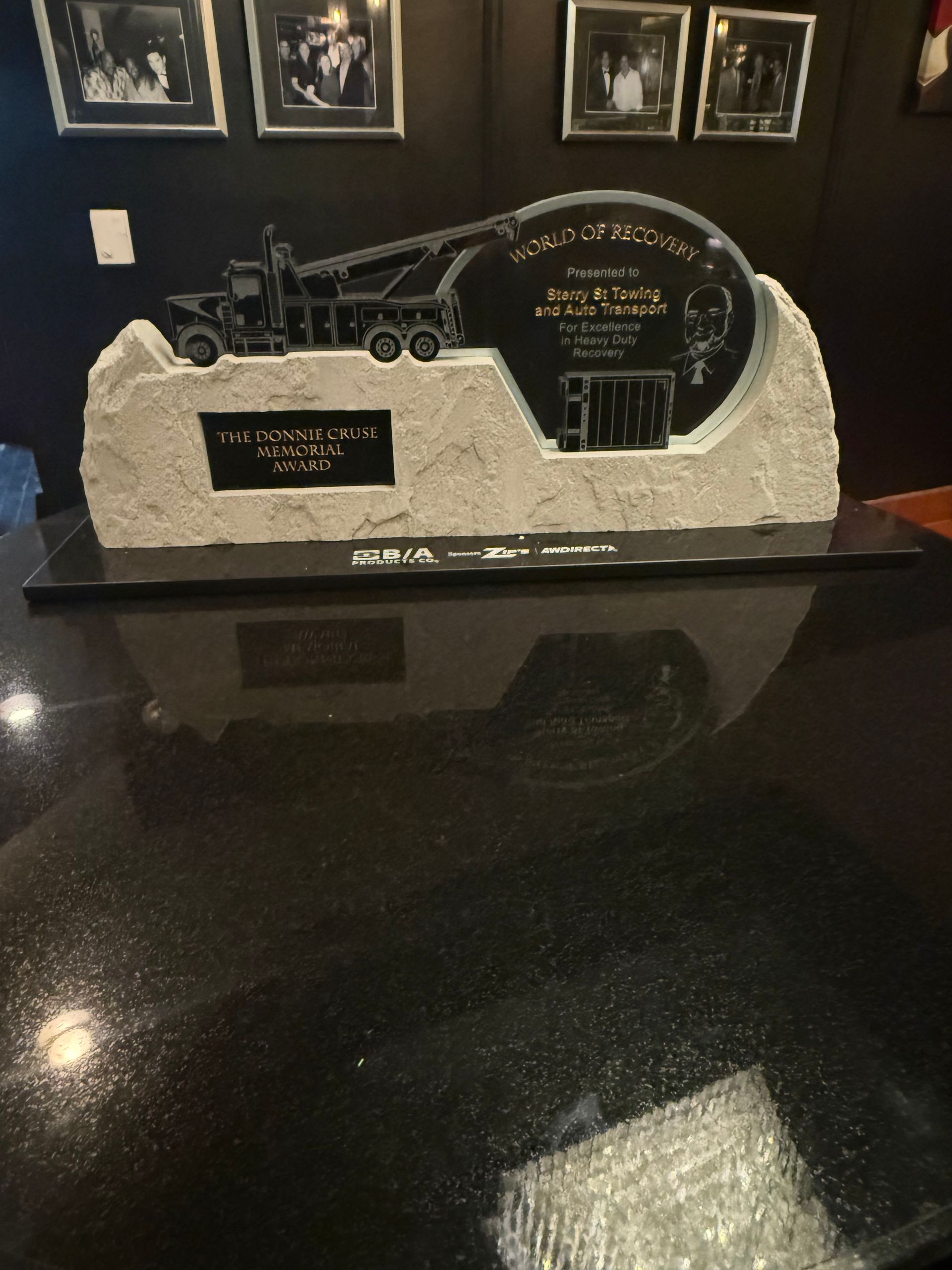Black memorial plaque with engraved truck and sign on a granite base, displayed indoors on a glossy table.