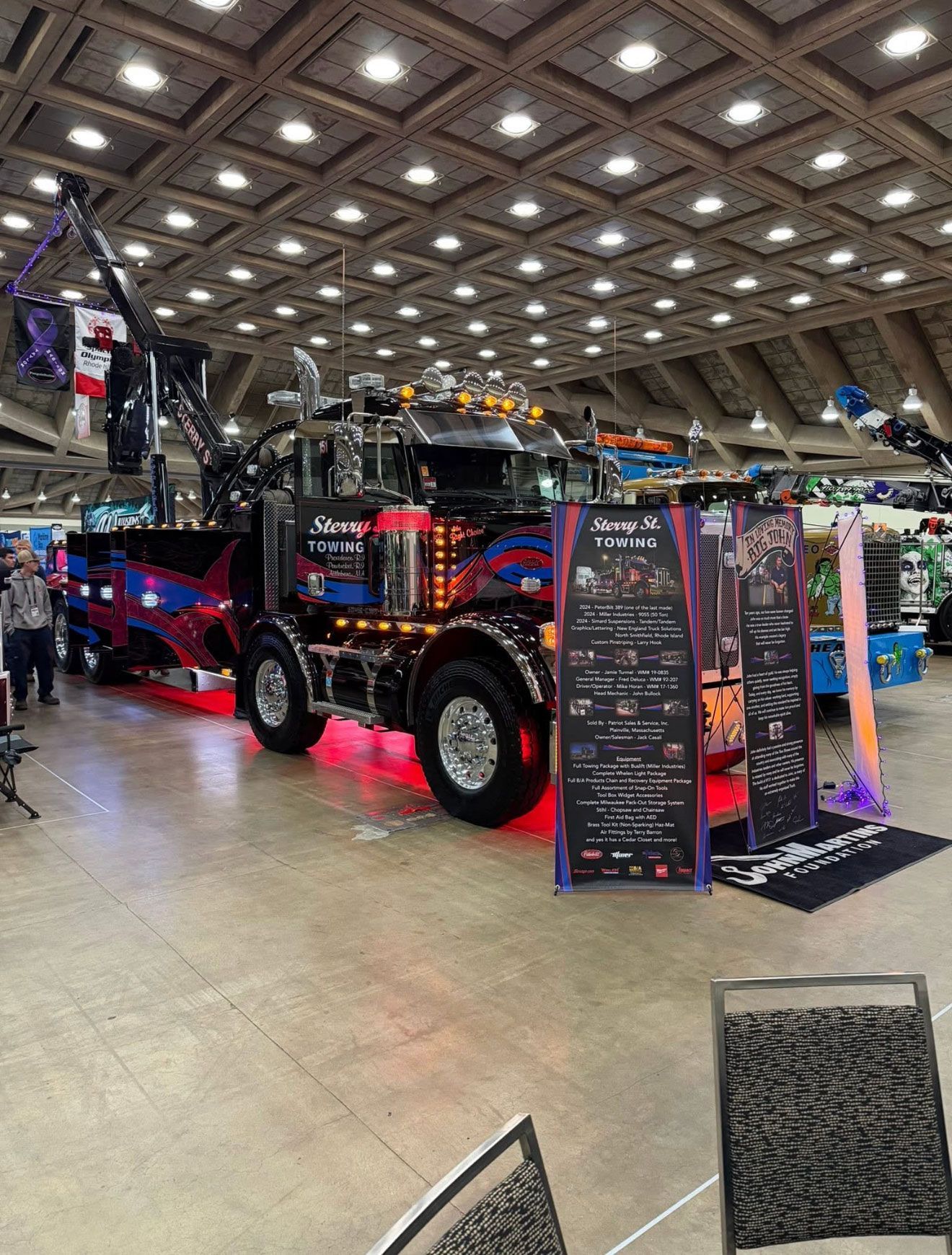Black custom semi truck at an indoor expo with red underglow and display signs.