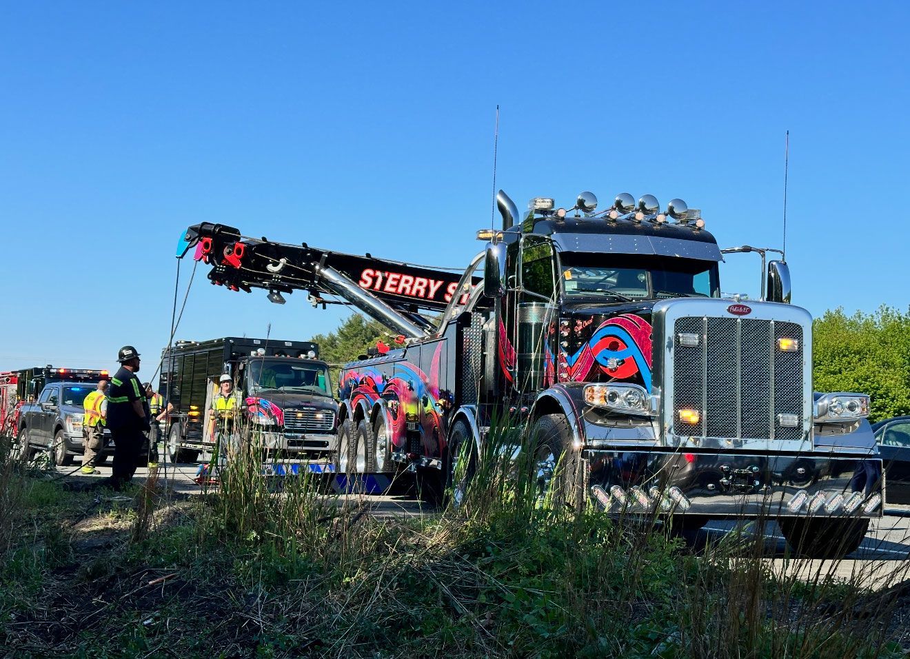 Fire truck with extended ladder at a roadside emergency scene under a clear blue sky.